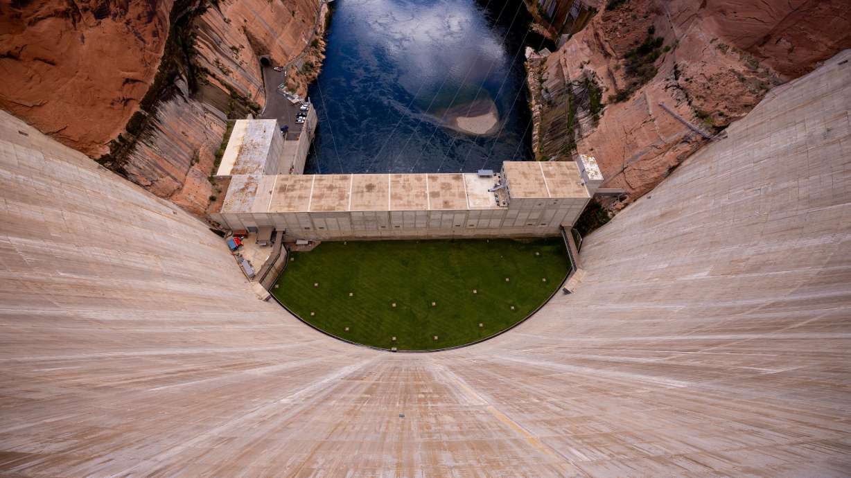 The curved concrete wall of Glen Canyon Dam stretches down to the Colorado River below in Page, Ariz., on Tuesday, July 19, 2022. Politics and threatened litigation is working to keep power generation at Glen Canyon and Hoover dams.