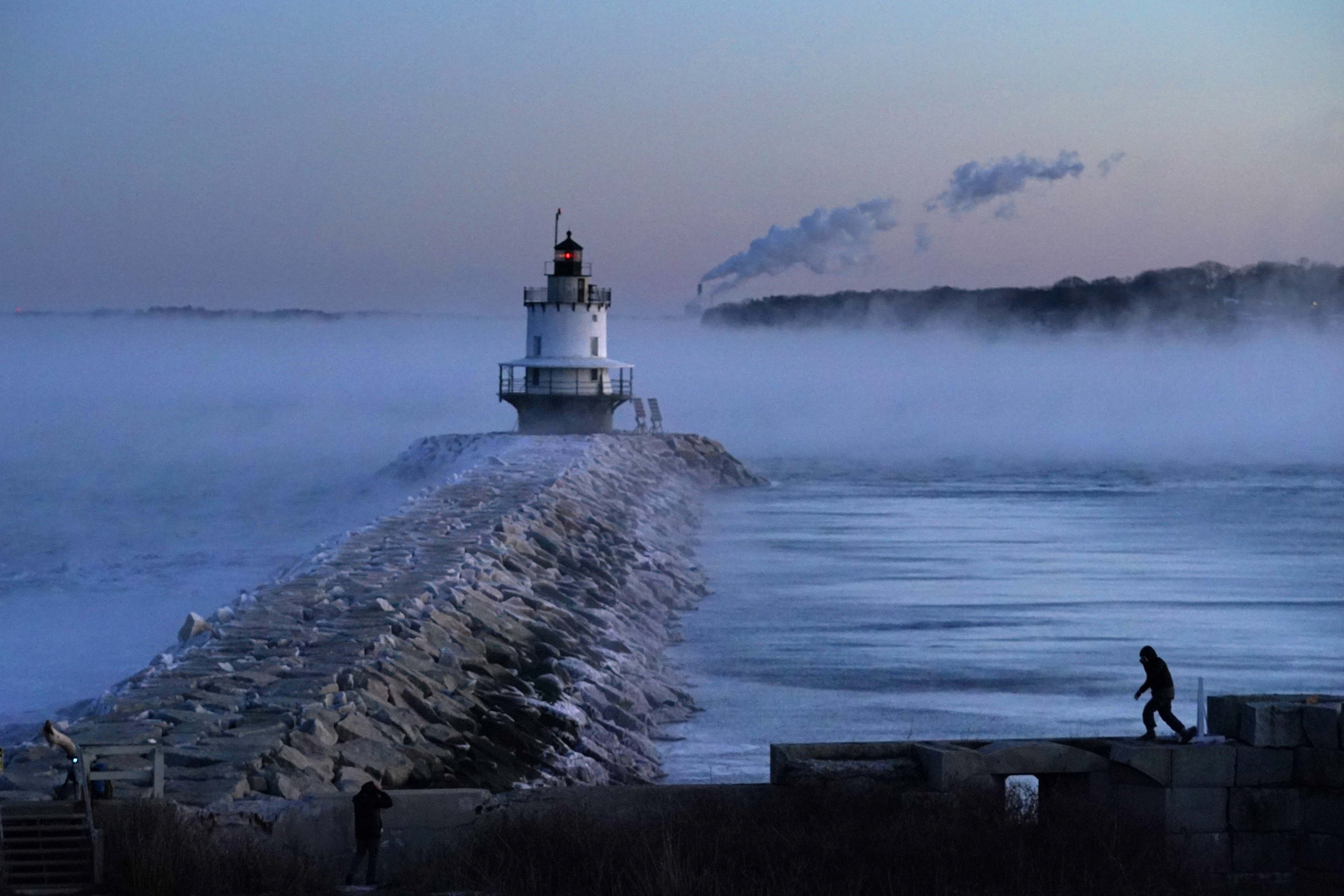 A man walks on sea wall near Spring Point Ledge Light, Saturday, in South Portland, Maine. The morning temperature was about -10 degrees Fahrenheit.