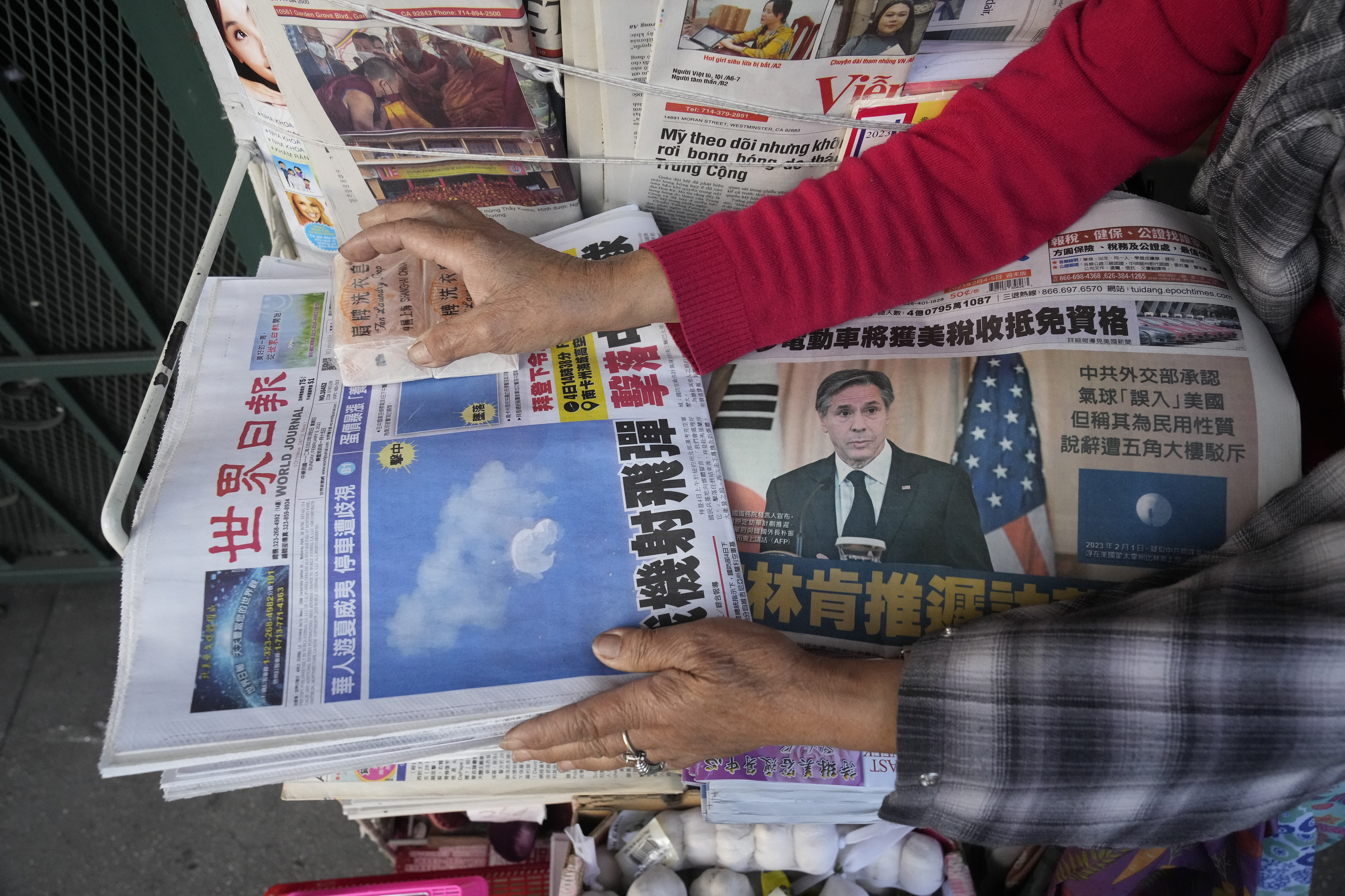 Business owner "Annie" weights down copies of the Chinese Daily News newspaper showcasing pictures of a suspected Chinese spy balloon, in the Chinatown district of Los Angeles Sunday.