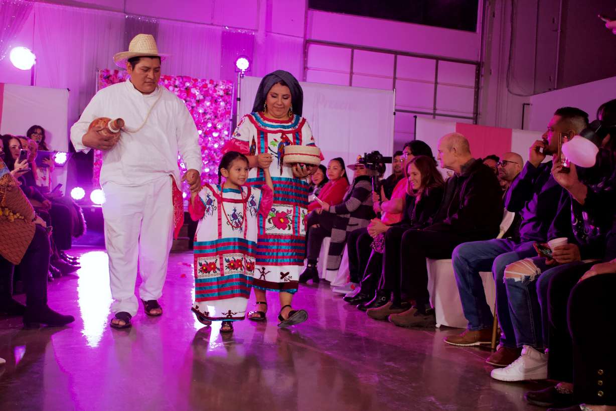 Ofelia Bazan, right, walks down the runway with her daughter, Itzy, and husband Francisco. The family it wearing clothing typical de La Cañada region of Oaxaca.