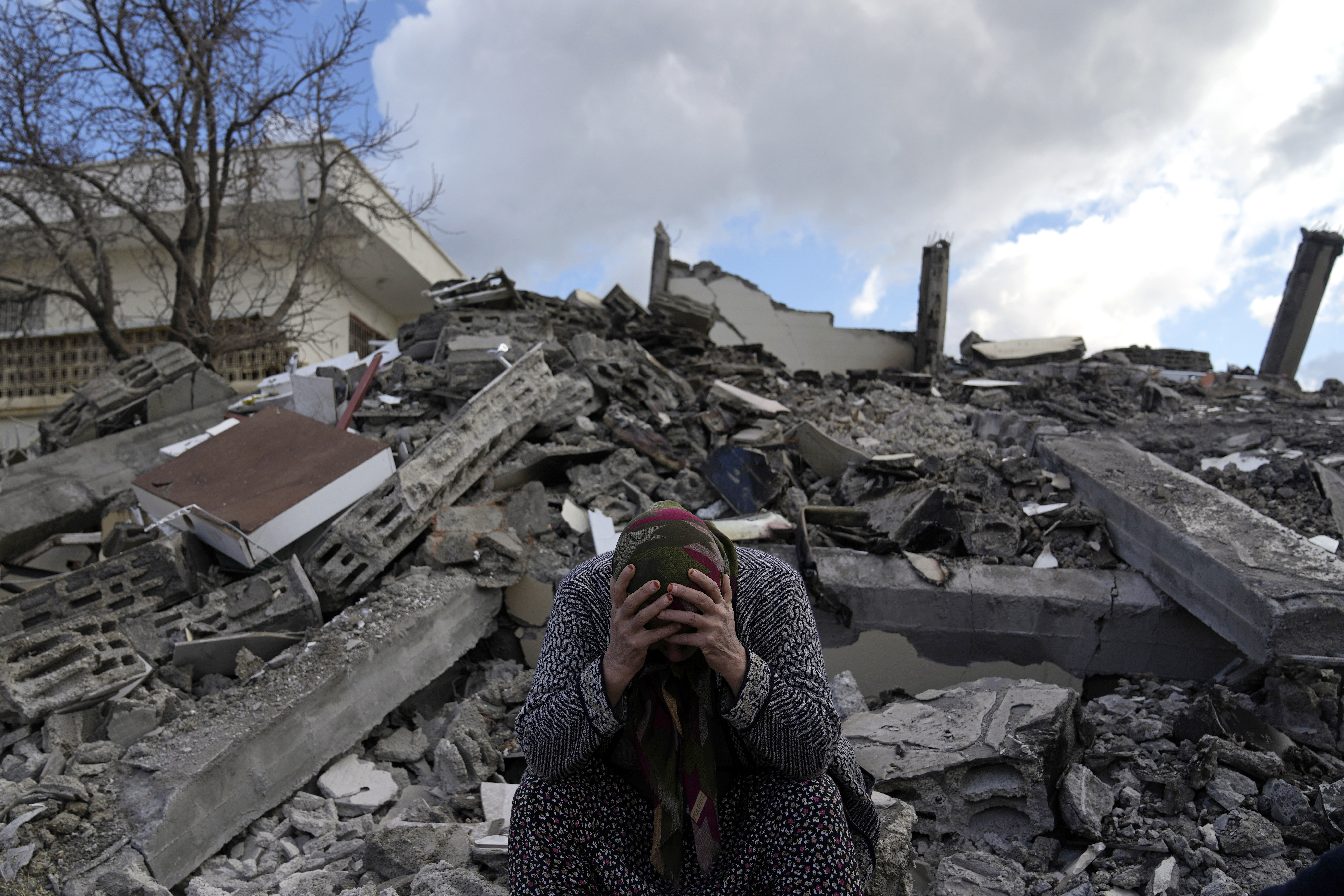 A woman sits on the rubble as emergency rescue teams search for people under the remains of destroyed buildings in Nurdagi town in southern Turkey, Tuesday.