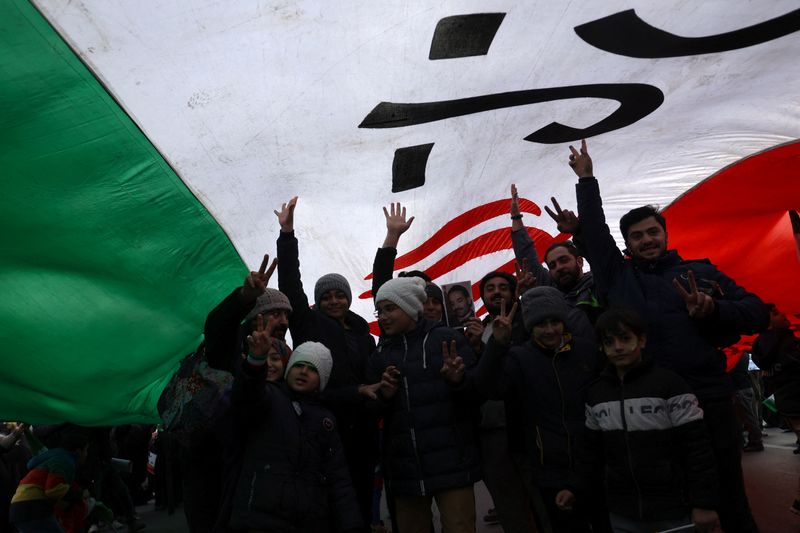 Iranians are seen under a large flag of Iran during the 44th anniversary of the Islamic Revolution in Tehran, Iran Saturday.