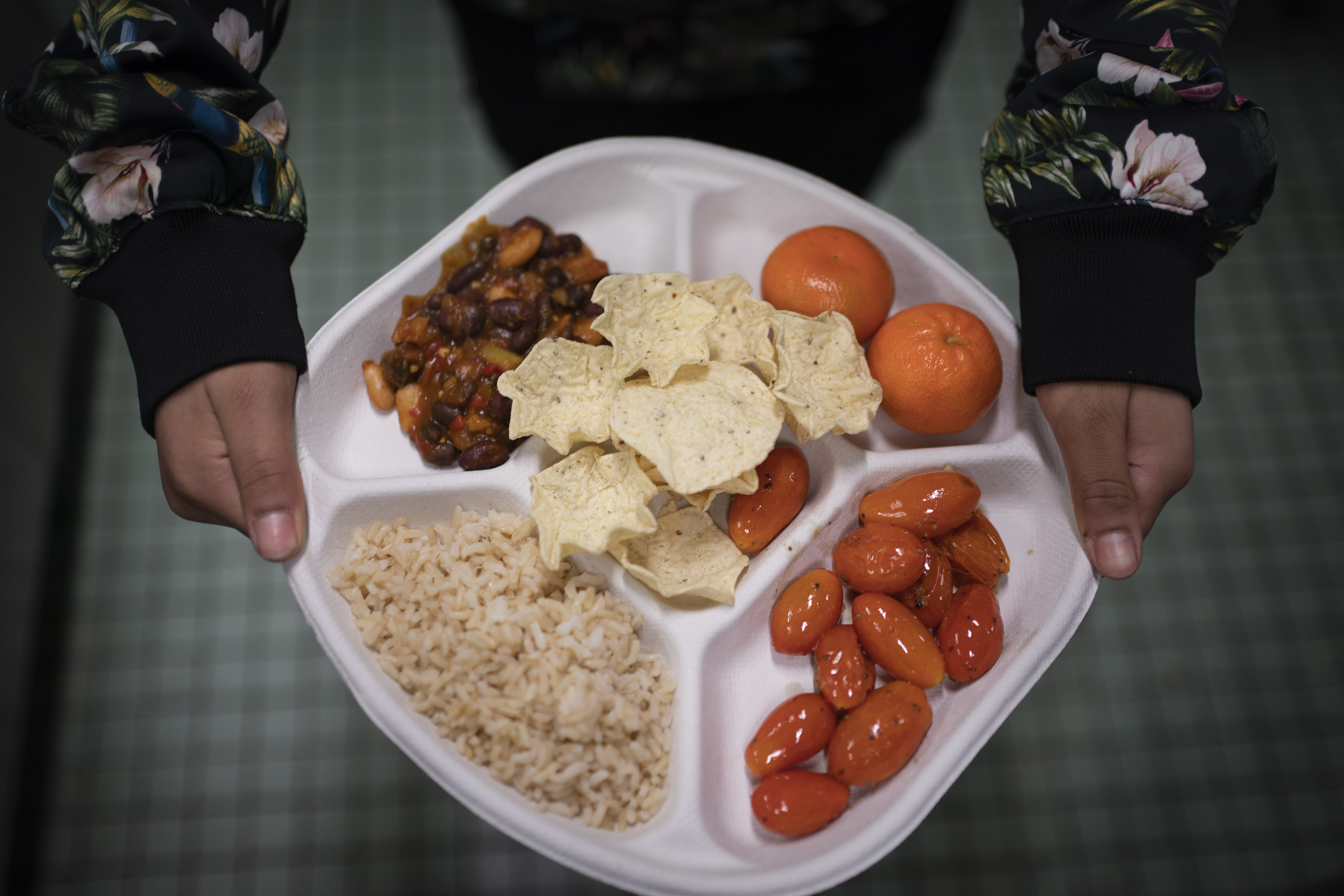 A seventh grader carries her plate which consists of three bean chili, rice, mandarins and cherry tomatoes and baked chips during her lunch break Saturday in Brooklyn. A 2010 federal law that boosted nutrition standards for school meals may have helped curb obesity among America’s children — even teenagers who can buy their own snacks, according to a new study.