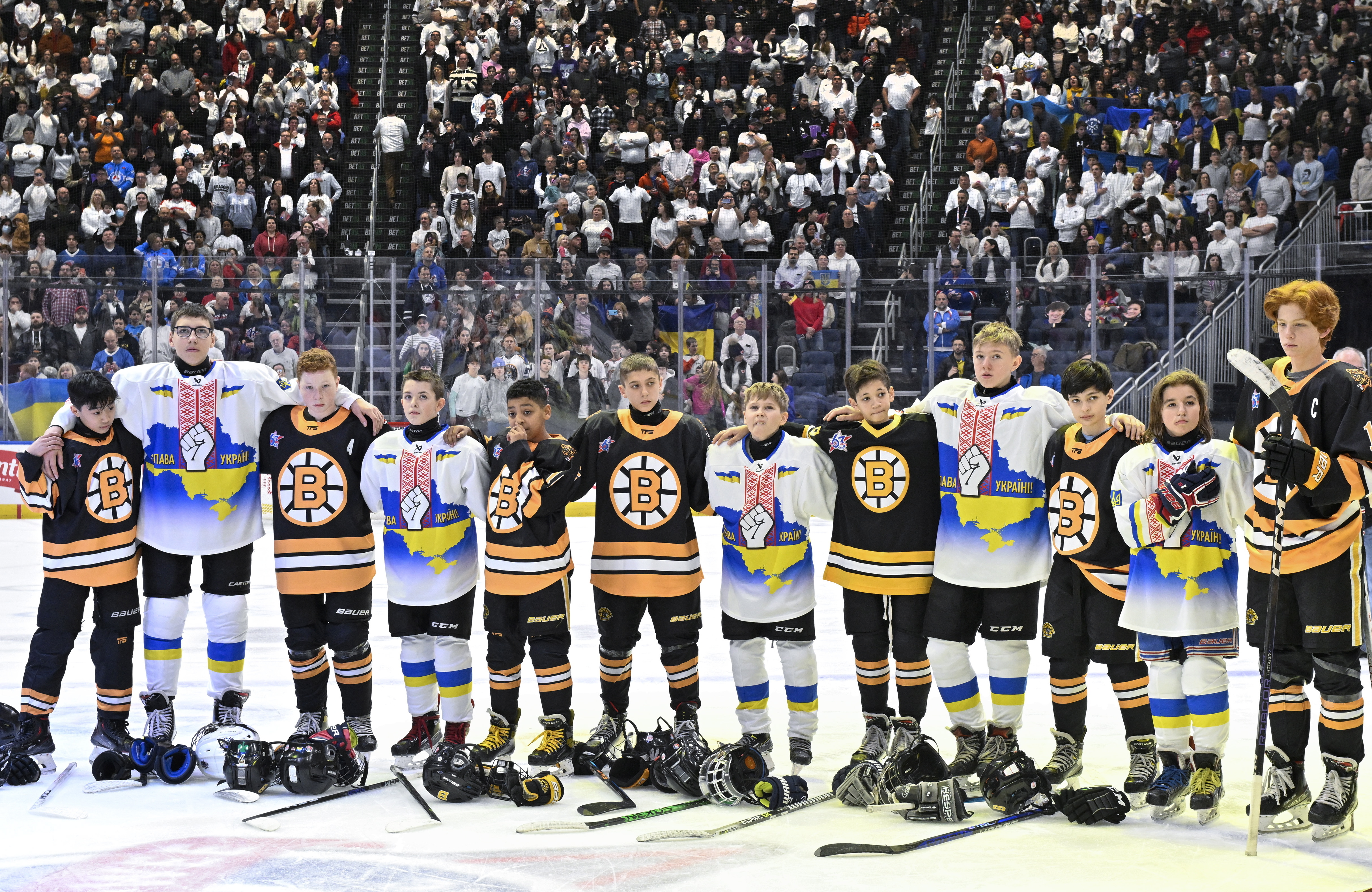 Team Ukraine Select and Boston Junior Bruins peewee teams stand together during the national anthems before their hockey game, Saturday, Feb. 11, 2023, in Quebec City. 