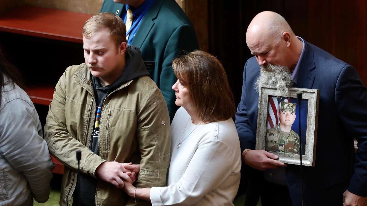 Craig Hicken, right, holds a photo of his son, Sgt. Erik Hicken, who served with the Utah National Guard. At left is Staff Sgt. Quinn Hicken, the brother of Erik Hicken, who is holding his mother Brenda Hicken’s hand during the 2022 Fallen Warriors ceremony at the Utah Legislature Friday.