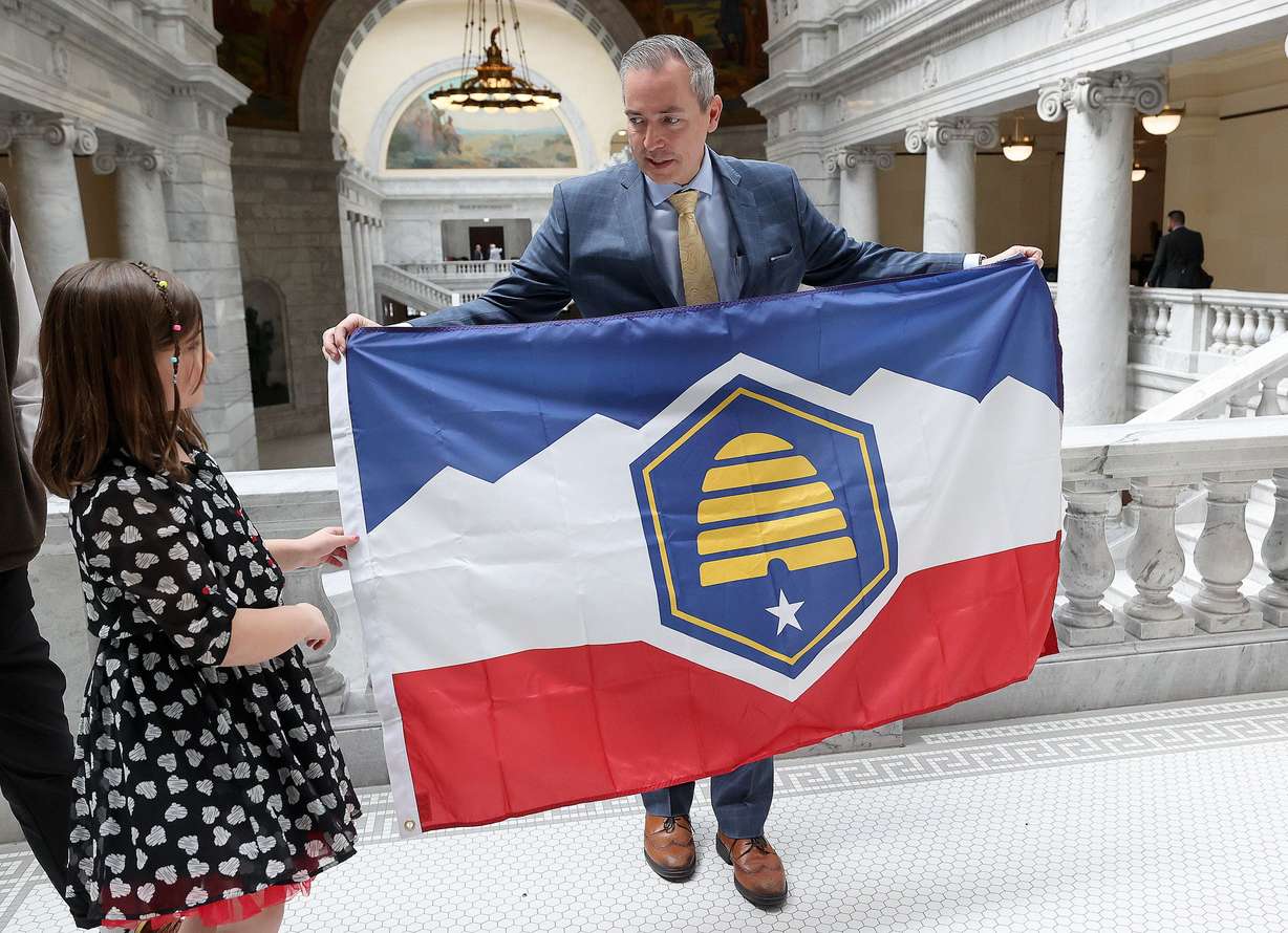 Savanna McCay helps her father Sen. Daniel McCay, R-Riverton, sponsor of SB31, State Flag Amendments, hold the new Utah state flag at the Capitol in Salt Lake City, on Thursday.