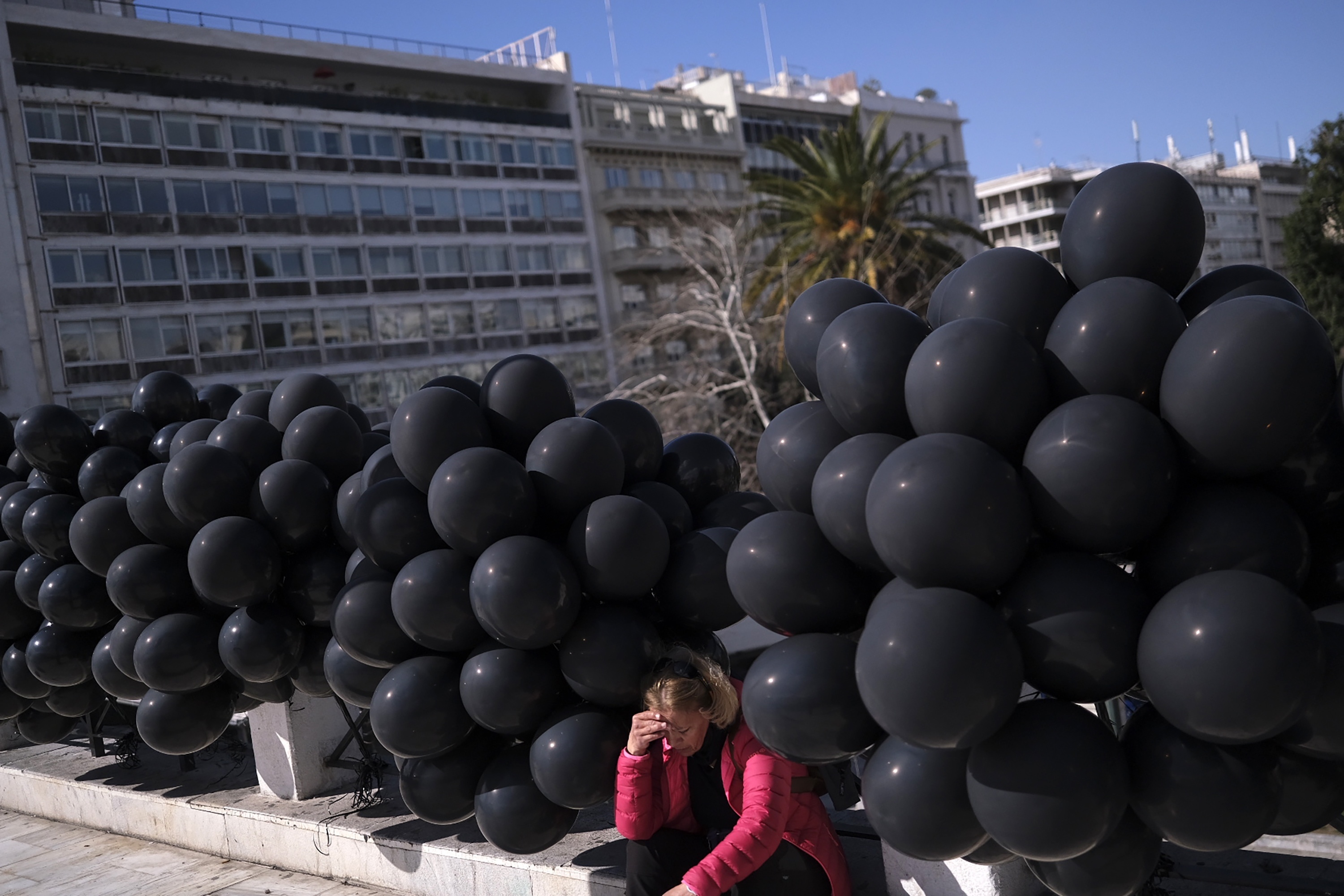 A woman sits among black balloons at a protest outside the Greek parliament, in Athens, Greece, Sunday. Thousands of protesters, take part in rallies around the country for the fifth day, protesting the conditions that led to the deaths of dozens of people late Tuesday, in Greece's worst recorded rail accident. 