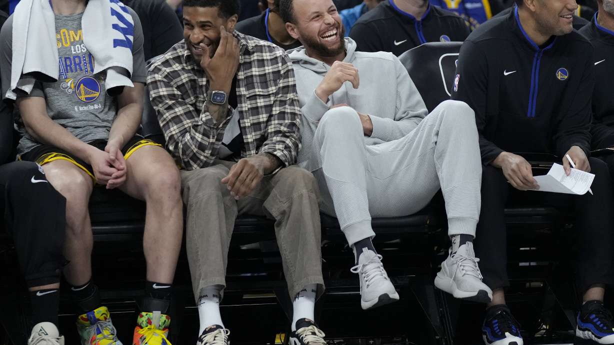 Golden State Warriors' Gary Payton II, middle left, laughs on the bench next to Stephen Curry during the first half of the team's NBA basketball game against the Los Angeles Clippers in San Francisco, Thursday, March 2, 2023.
