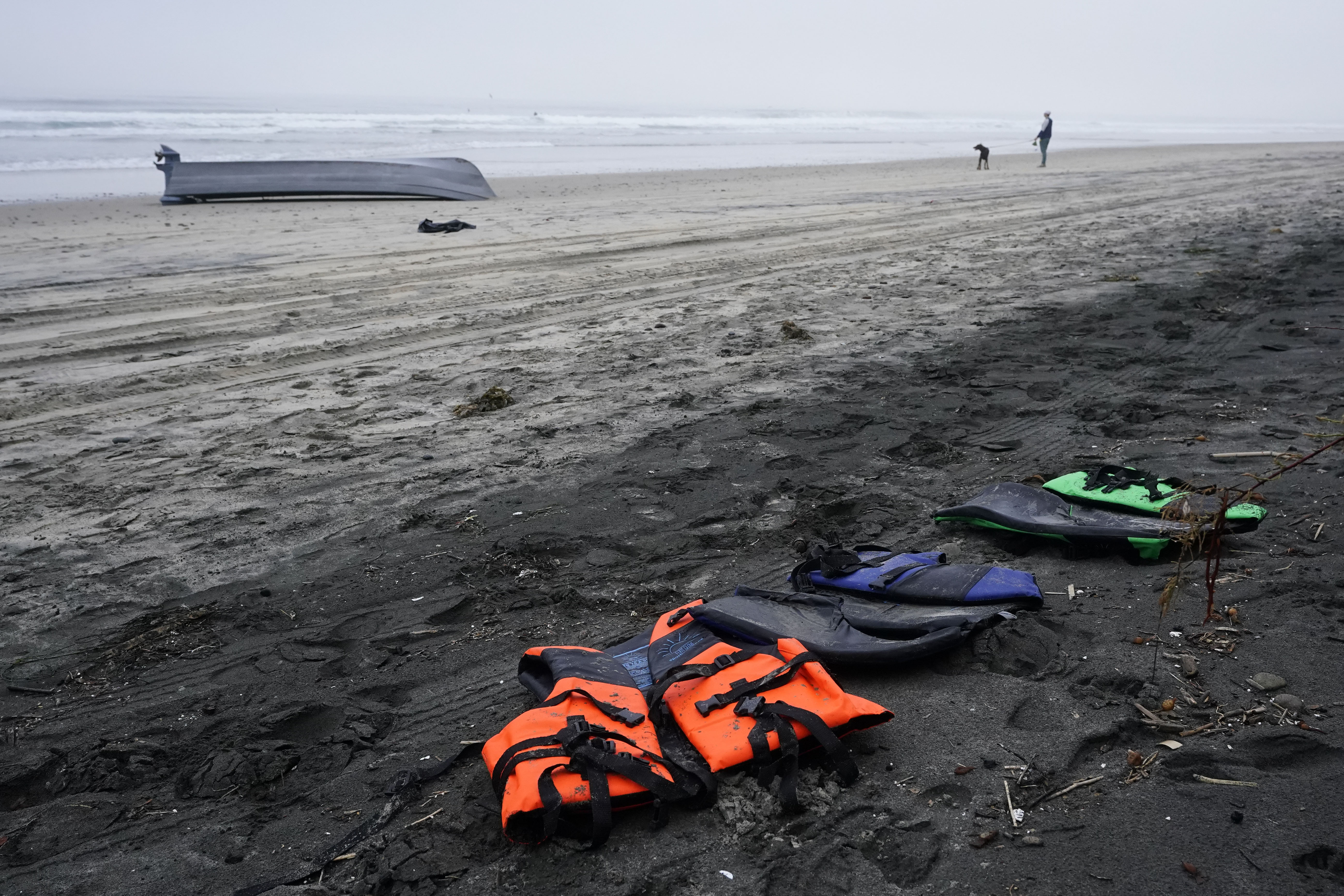 A boat sits overturned near a row of life jackets on Blacks Beach, Sunday, in San Diego. Authorities say multiple people died when two suspected smuggling boats overturned off the coast San Diego, and crews were searching for additional victims.
