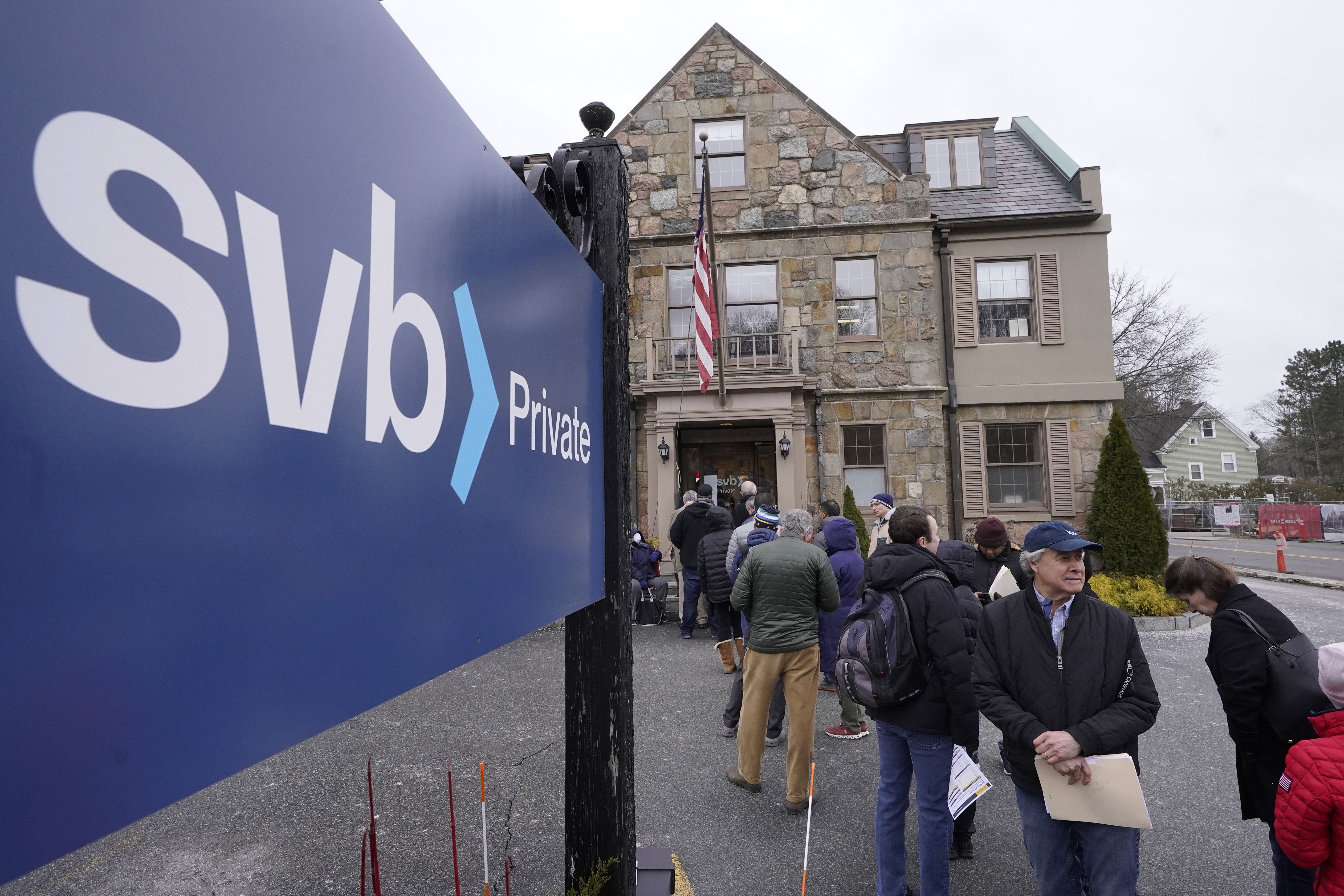 Customers and bystanders form a line outside a Silicon Valley Bank branch location, Monday, in Wellesley, Mass. Lawmakers across the country reacted to federal action over Silicon Valley Bank.