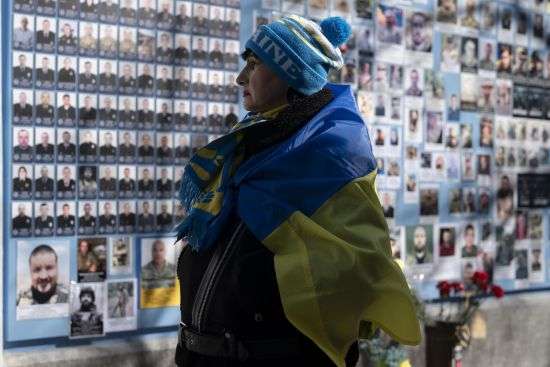 A woman wrapped in a Ukrainian flag stands next to the Memory Wall of Fallen Defenders of Ukraine in the Russian-Ukrainian War on Ukrainian Volunteer Day in Kyiv, Ukraine, Tuesday.