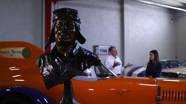 A statue of Ab Jenkins sits in front of the Mormon Meteor III at the Price Museum of Speed, as Ab Jenkins II stands behind the race car.
