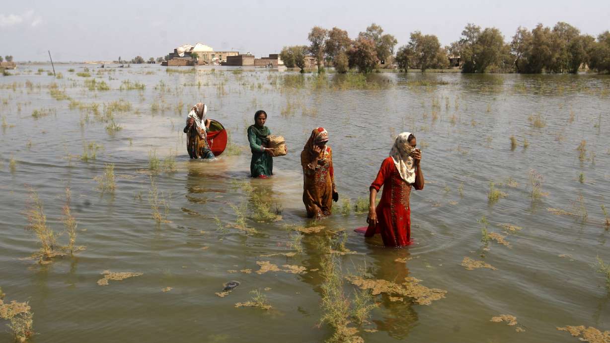 Pakistani women wade through floodwaters in Shikarpur district of Sindh Province, of Pakistan, Sept. 2, 2022. A major new United Nations report released Monday, provides a sobering reminder that time is running out if humanity wants to avoid passing a dangerous global warming threshold.