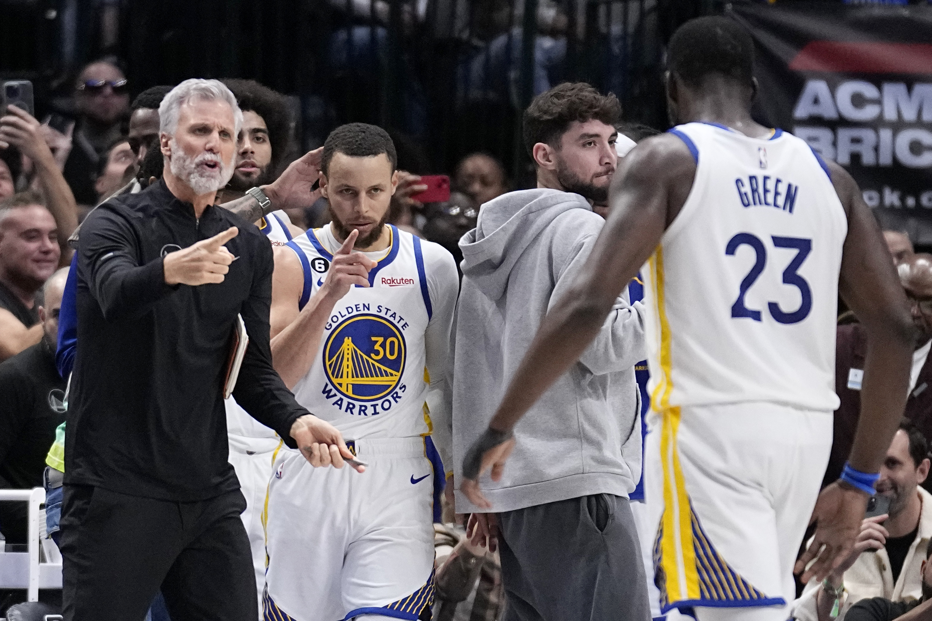 Golden State Warriors guard Stephen Curry (30) and Draymond Green (23), along with staff, celebrate a basket late in the second half of an NBA basketball game against the Dallas Mavericks, Wednesday, March 22, 2023, in Dallas.