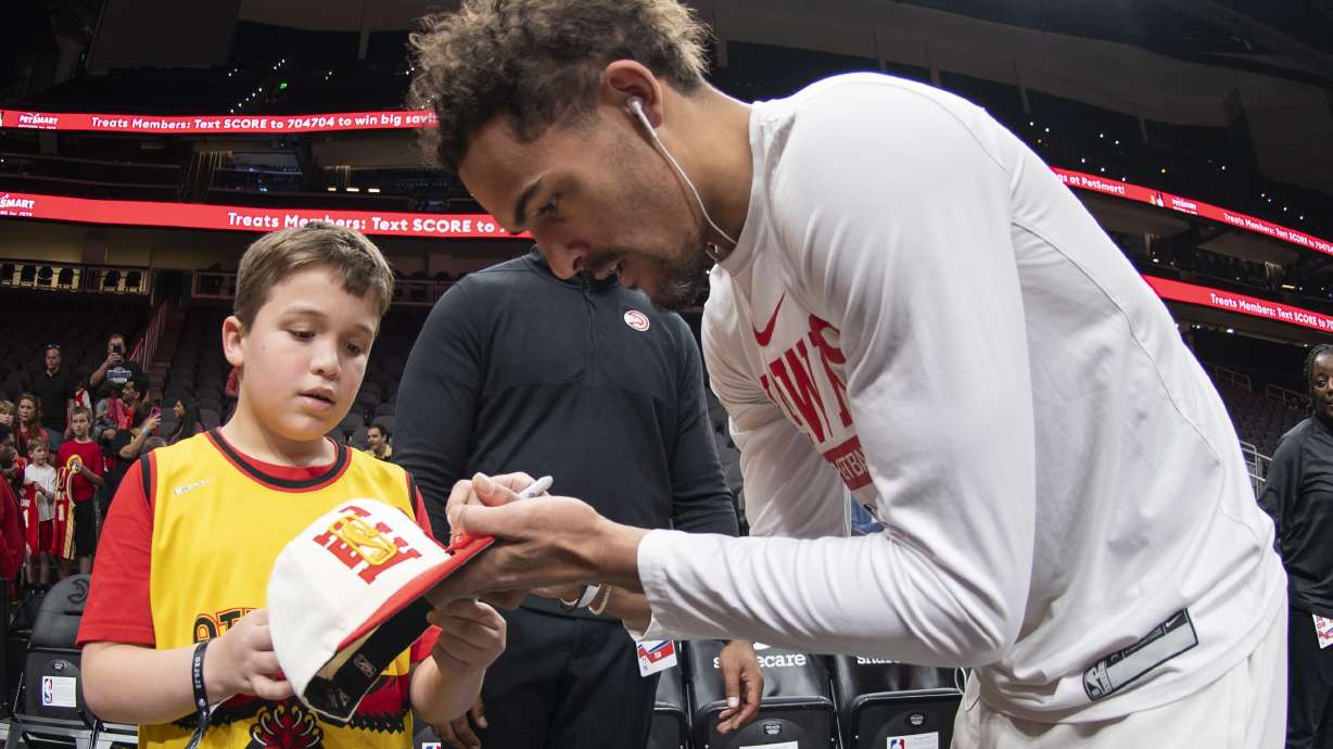 Atlanta Hawks guard Trae Young signs an autograph for a young fan before an NBA basketball game against the Indiana Pacers, Saturday, March 25, 2023, in Atlanta.