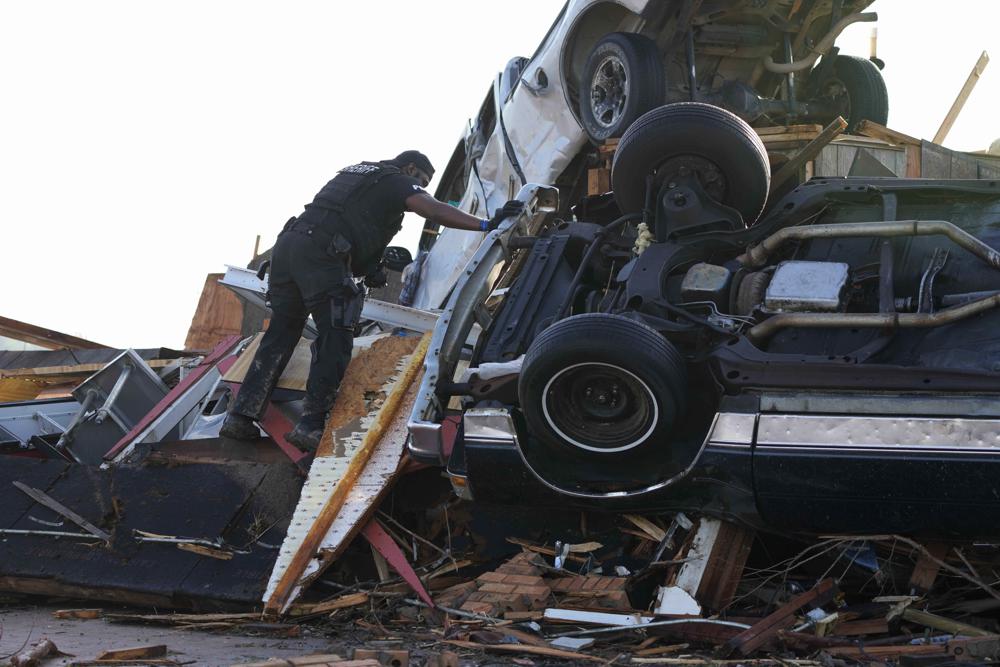 A sheriff's deputy climbs onto a pile of wind-tossed vehicles to search for survivors or the deceased at Chuck's Dairy Bar in Rolling Fork, Mississippi, Saturday.