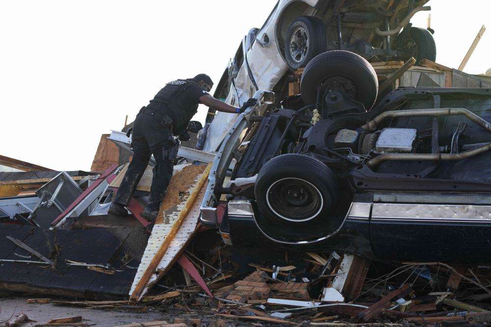 A sheriff's deputy climbs onto a pile of wind-tossed vehicles to search for survivors or the deceased at Chuck's Dairy Bar in Rolling Fork, Mississippi, Saturday.