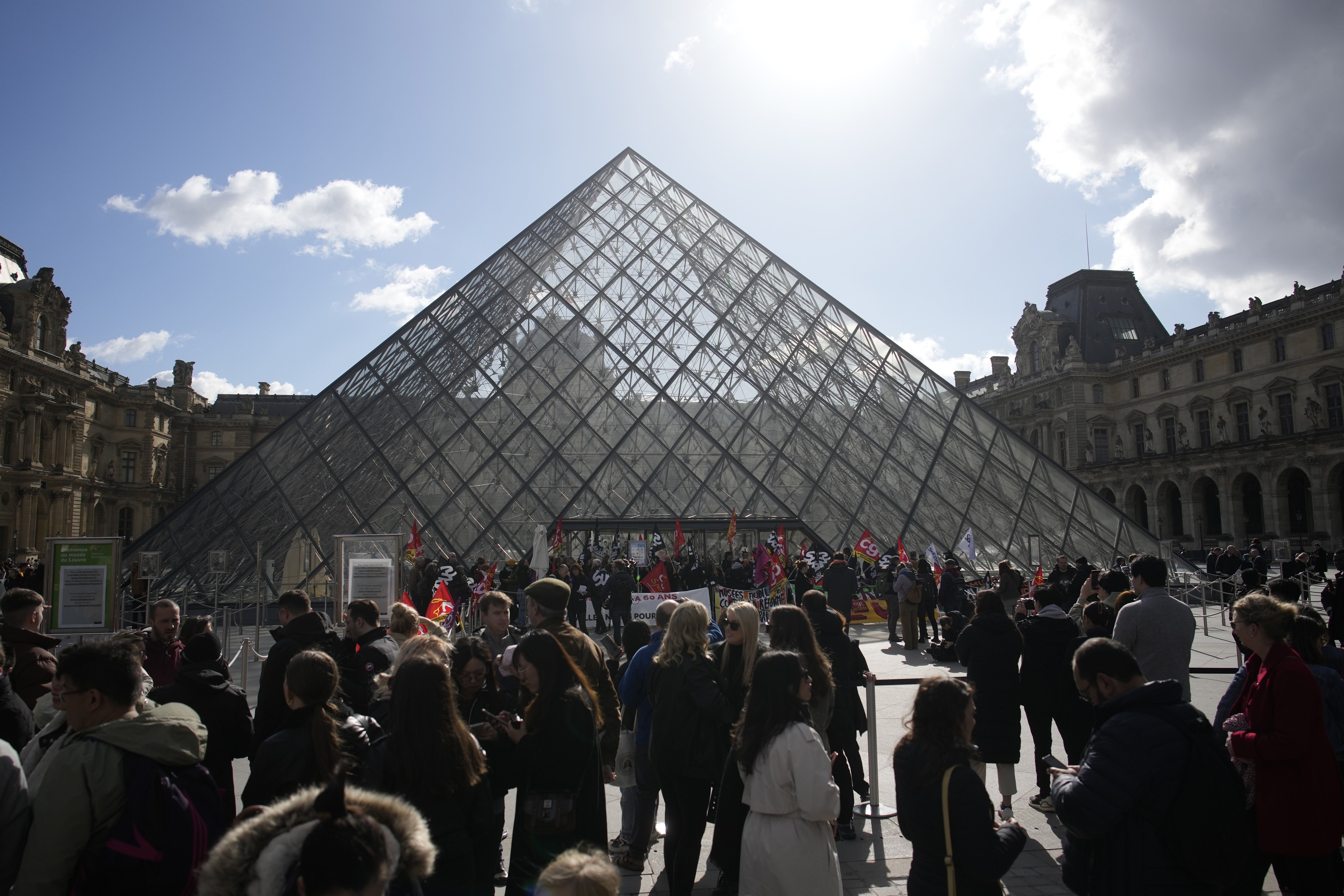 Visitors wait as workers of the culture industry demonstrate outside the Louvre museum Monday in Paris. President Emmanuel Macron inflamed public anger by sending his already unpopular plan to raise the retirement age by two years, from 62 to 64, through parliament without a vote.