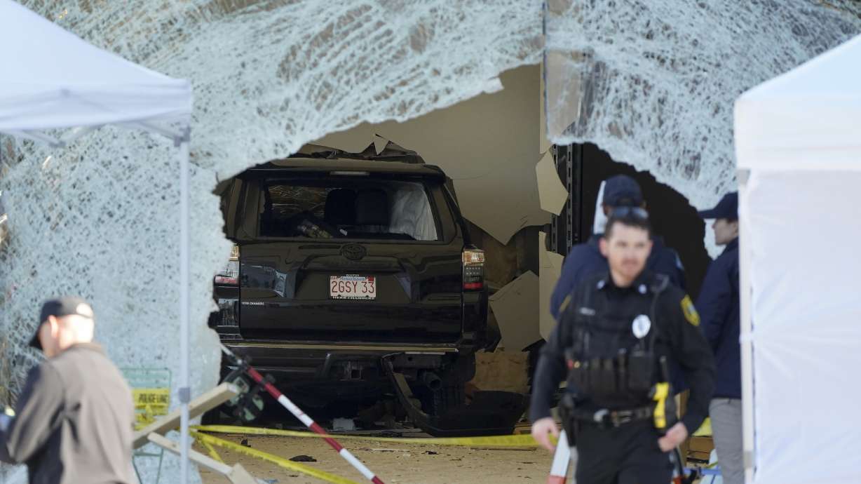 An SUV rests inside an Apple store behind a large hole in the glass front of the store on Nov. 21, 2022, in Hingham, Mass. The Massachusetts man whose SUV crashed through the glass storefront, killing one man and injuring nearly two dozen other people, now faces a murder charge.