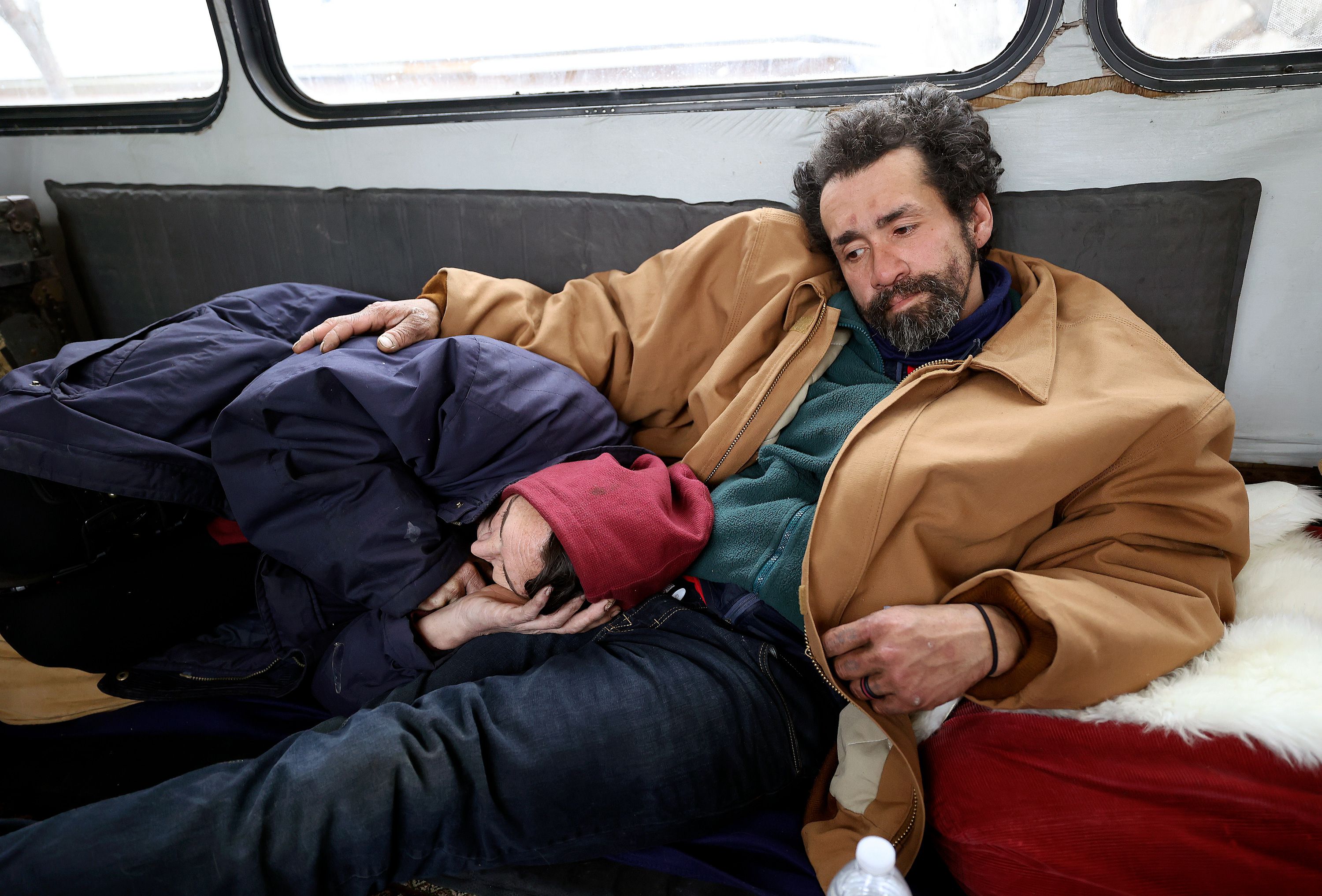 Barbara Elmer rests on the lap of Mike “Trigger” Garcia on the Nomad Alliance bus, temporarily parked outside a meetinghouse of The Church of Jesus Christ of Latter-day Saints, that is not in use, in Salt Lake City, on March 8.