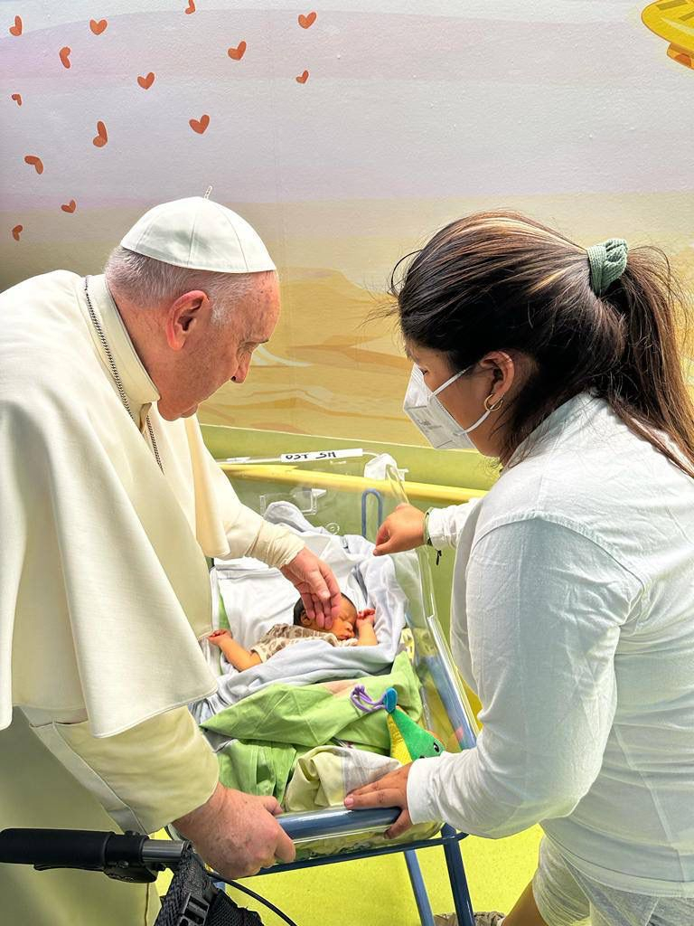 In this image made available by Vatican Media, Pope Francis caresses an infant before baptizing him with the name of Miguel Angel, Friday inside the Agostino Gemelli University Hospital where he is treated since Wednesday for a bronchitis. Francis is expected to be discharged on Saturday.