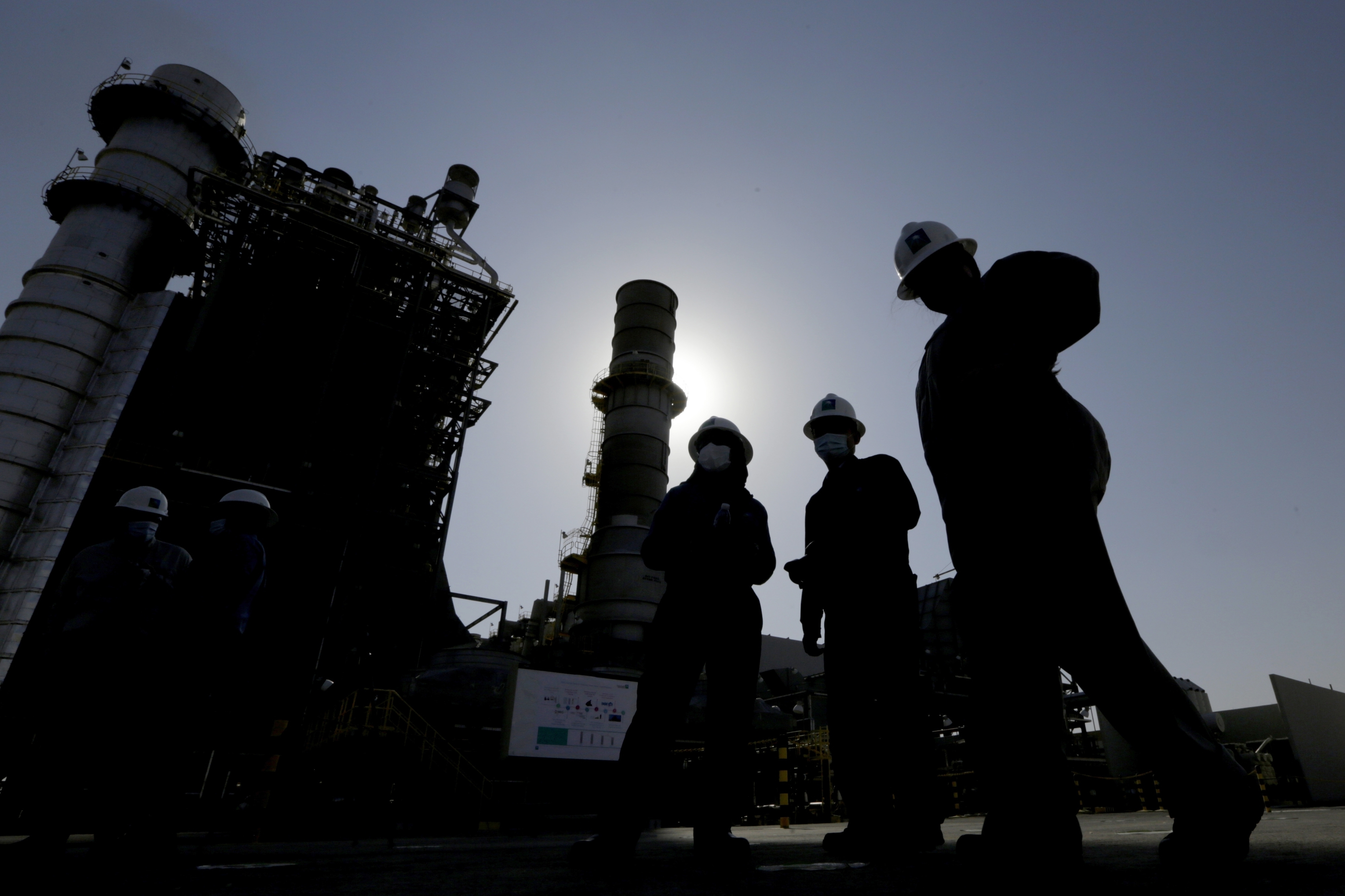 Saudi Aramco engineers walk in front of a gas turbine generator at Khurais oil field during a tour in Saudi Arabia on June 28, 2021. Saudi Arabia said Sunday it will cut oil production by 500,000 barrels per day from May until the end of 2023. 