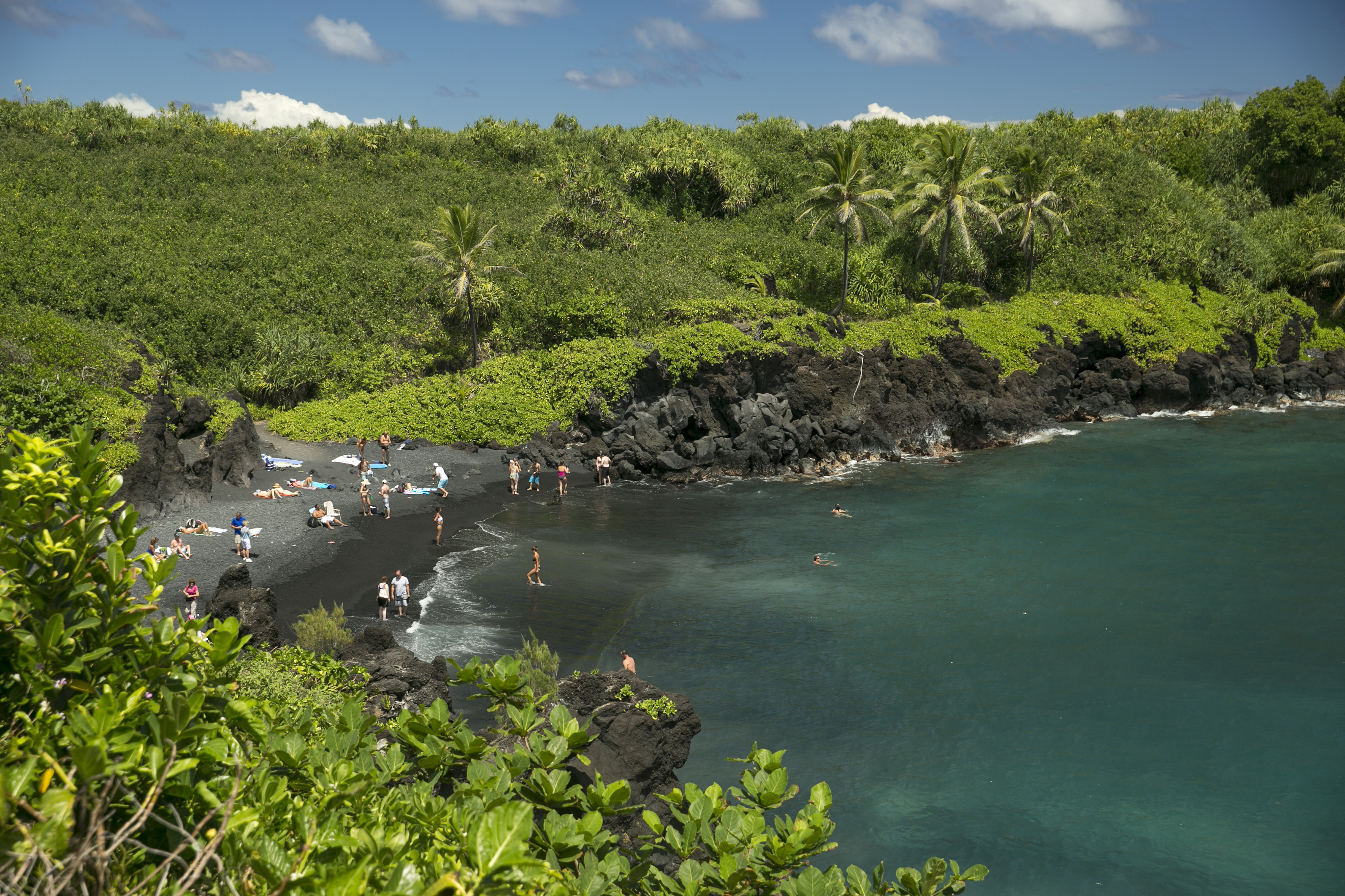 People spend time on the black sand beach at Waianapanapa State Park in Hana, Hawaii, on Sept. 24, 2014. Taking care of Hawaii's unique natural environment costs money and now the state wants tourists to help pay for it.