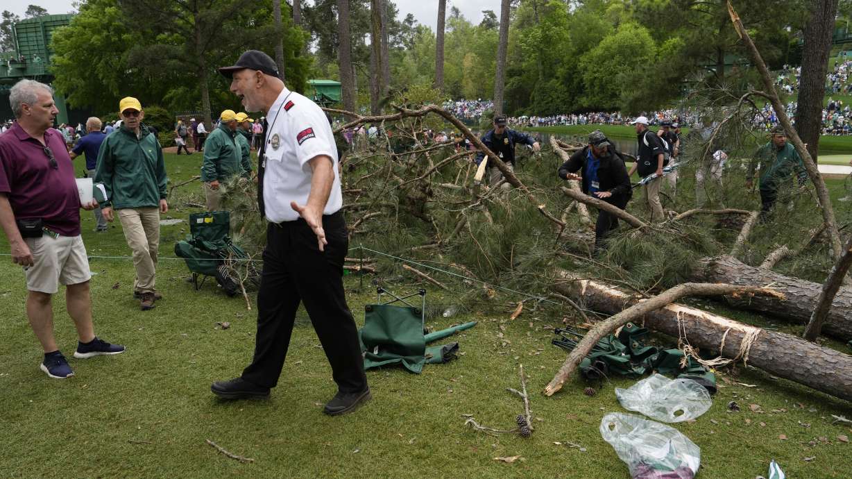 A security guard moves patrons away from trees that blew over on the 17th hole during the second round of the Masters golf tournament at Augusta National Golf Club on Friday, April 7, 2023, in Augusta, Ga.
