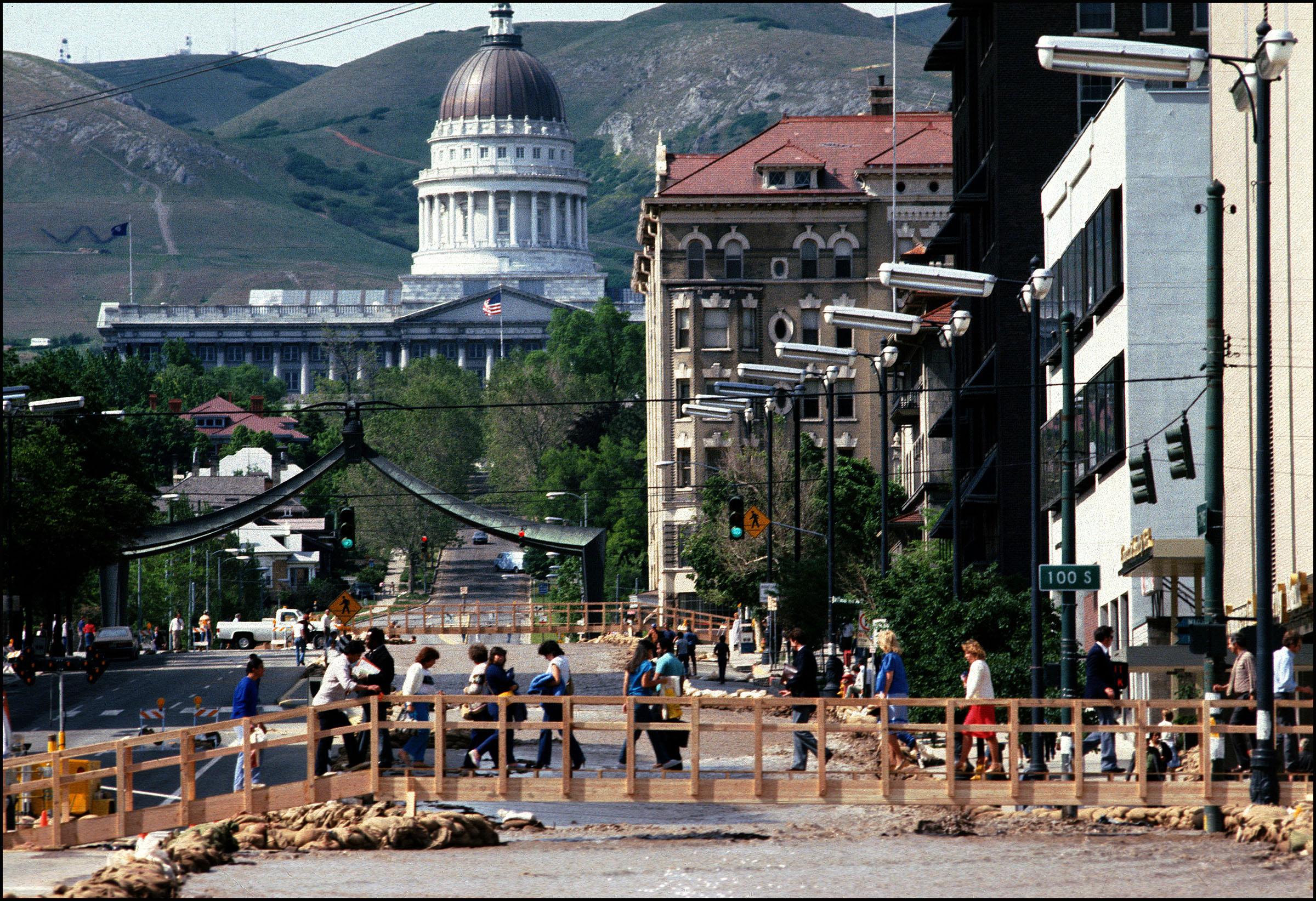 People cross a makeshift bridge over a flooded State Street in Salt Lake City in 1983. The river was the result of massive debris buildup that blocked four blocks worth of pipes beginning by the mouth of City Creek Canyon.