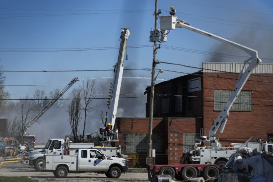 Utility workers remove utilities from the area as firefighter pour water on an industrial fire in Richmond, Ind., Wednesday. Authorities urged people to evacuate if they live near the fire. The former factory site was used to store plastics and other materials for recycling or resale.