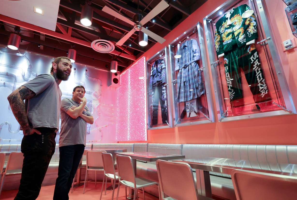 Post Malone and Raising Cane’s founder Todd Graves show media around a remodeled Raising Cane’s Restaurant, designed by the singer, in Midvale on Thursday. Outfits that Post Malone wore on tour hang on the wall.