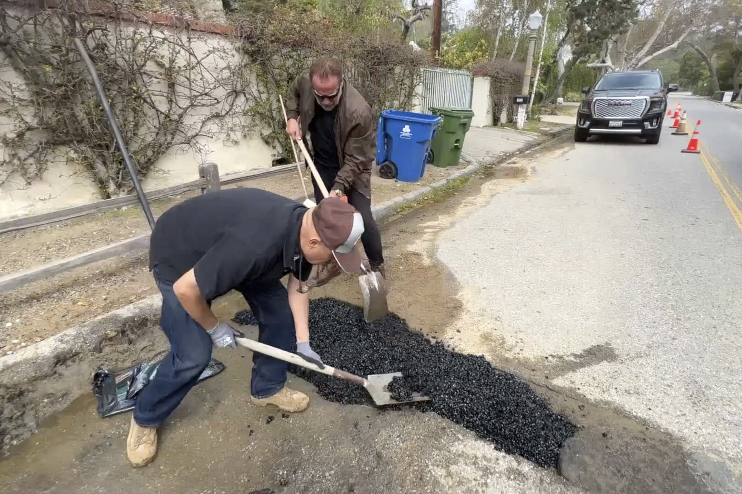 This video still image provided by The Office of Arnold Schwarzenegger, shows former California Governor Arnold Schwarzenegger, center back, repairing a pot hole on a street in his Los Angeles neighborhood on April 11. Fed up by an enormous pothole in his neighborhood, Schwarzenegger picked up a shovel and filled it himself. 