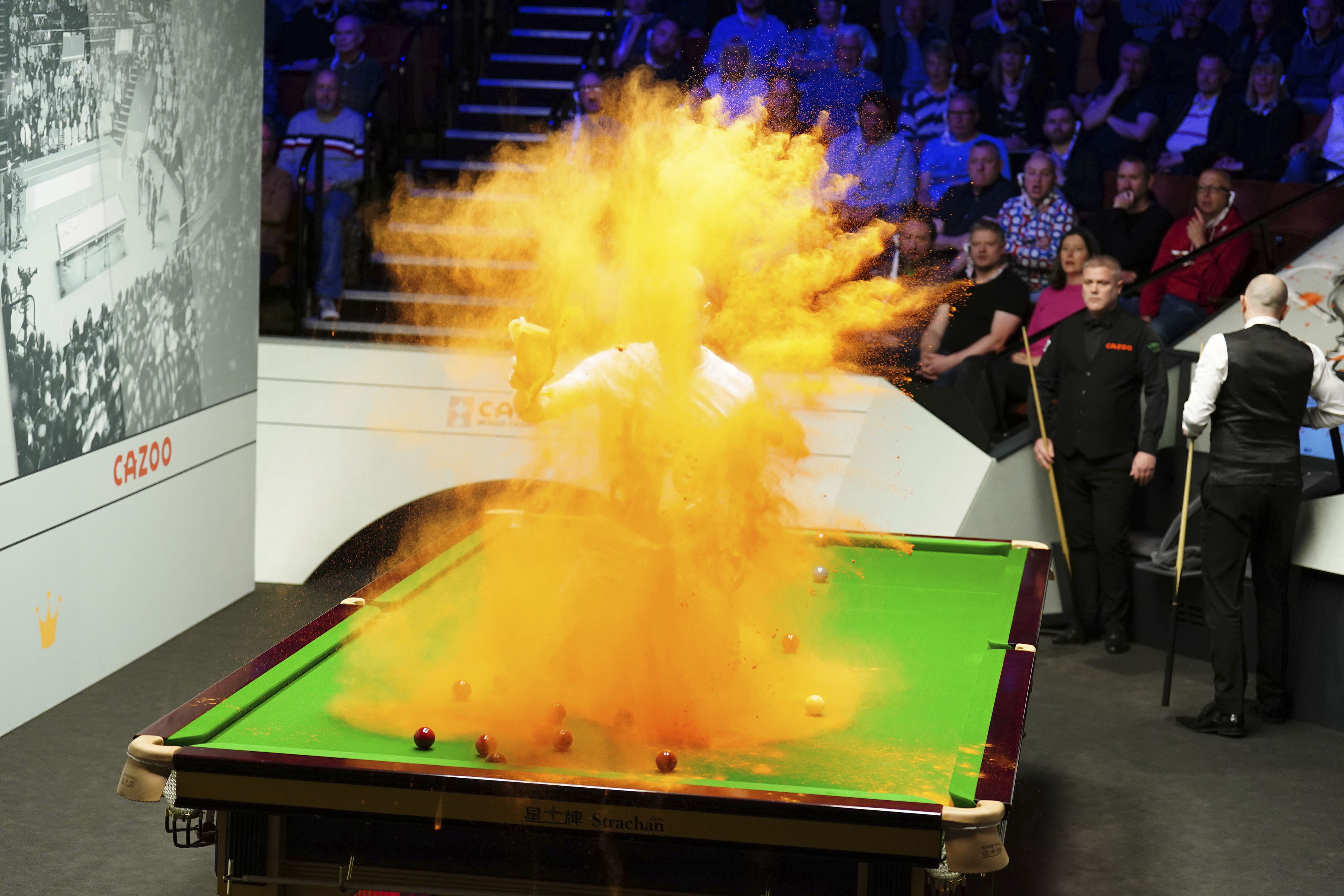 A 'Just Stop Oil' protester jumps on the table and throws orange powder during the match between Robert Milkins against Joe Perry as part of day three of the World Snooker Championship at the Crucible Theatre, Sheffield, Britain, Monday, April 17, 2023. 