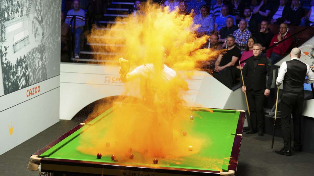 A 'Just Stop Oil' protester jumps on the table and throws orange powder during the match between Robert Milkins against Joe Perry as part of day three of the World Snooker Championship at the Crucible Theatre, Sheffield, Britain, Monday, April 17, 2023.