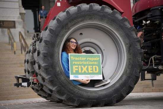 Colorado Rep. Brianna Titone sits in the wheel of a tractor on display before Colorado Gov. Jared Polis signed legislation that forces manufacturers to provide the necessary manuals, tools, parts and even software to farmers so they can fix their own machines Tuesday during a ceremony outside the State Capitol in downtown Denver.
