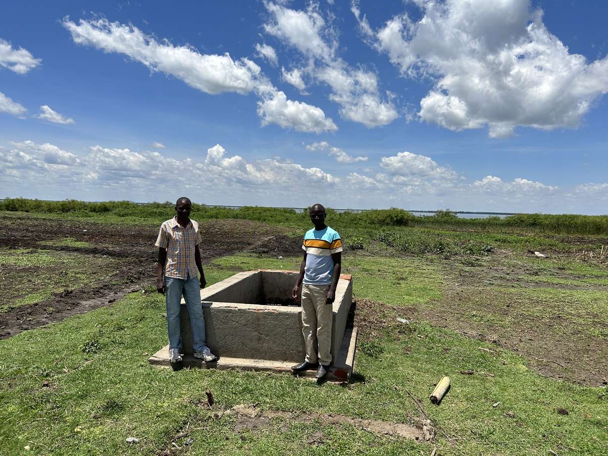 Godfrey Lufafa and a village member stand next to a stone cistern that was built to breed weevils to help clean Lake Nakuwa in Uganda in April 2023.