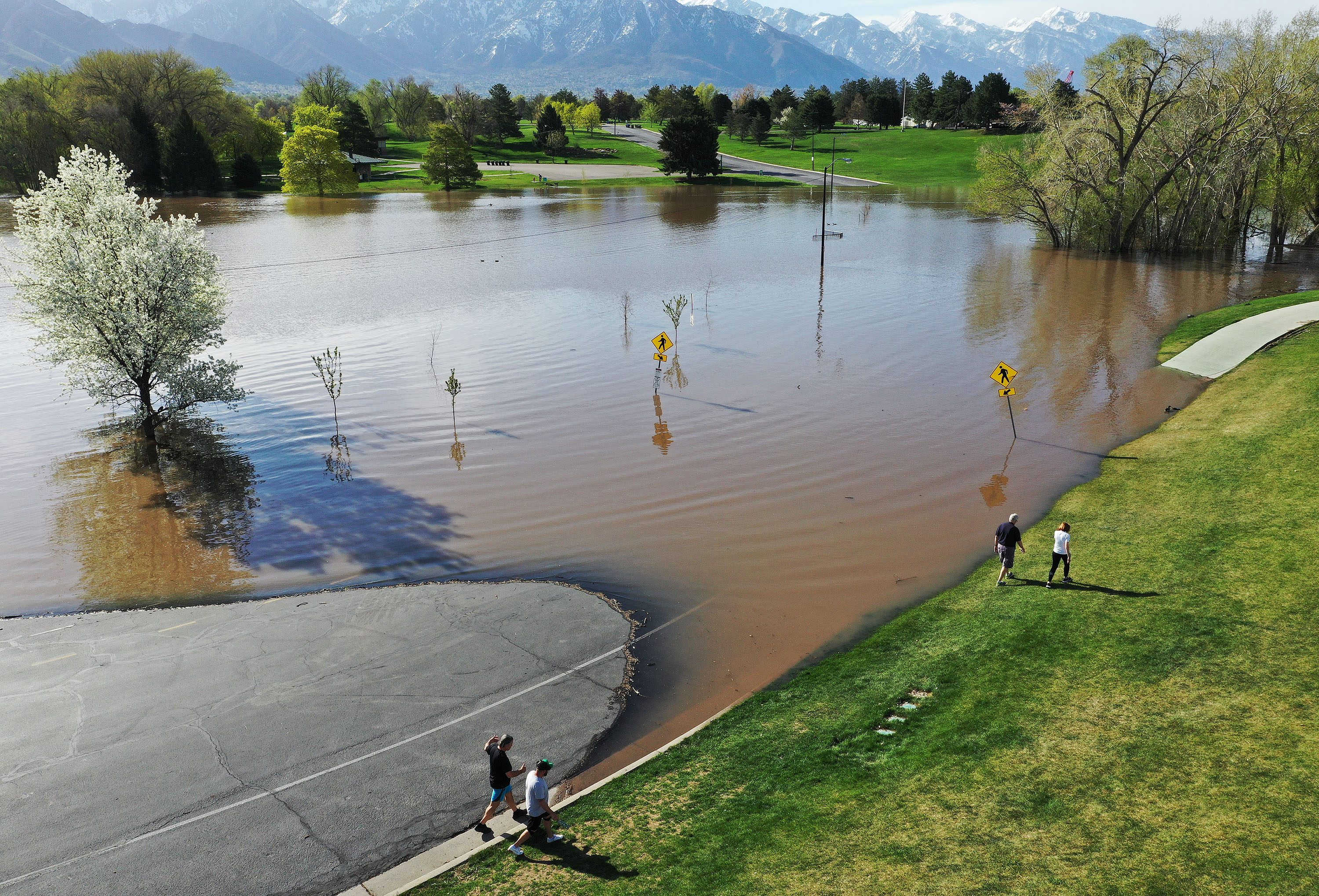 Walkers go around the flooded road where a pond has formed in Sugarhouse Park in Salt Lake City on Tuesday. Flood warnings have been put in place for rivers around the valley. 