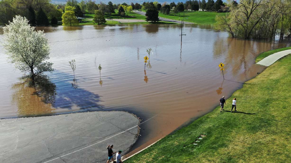 Walkers go around the flooded road where a pond has formed in Sugarhouse Park in Salt Lake City on Tuesday. Flood warnings have been put in place for rivers around the valley.