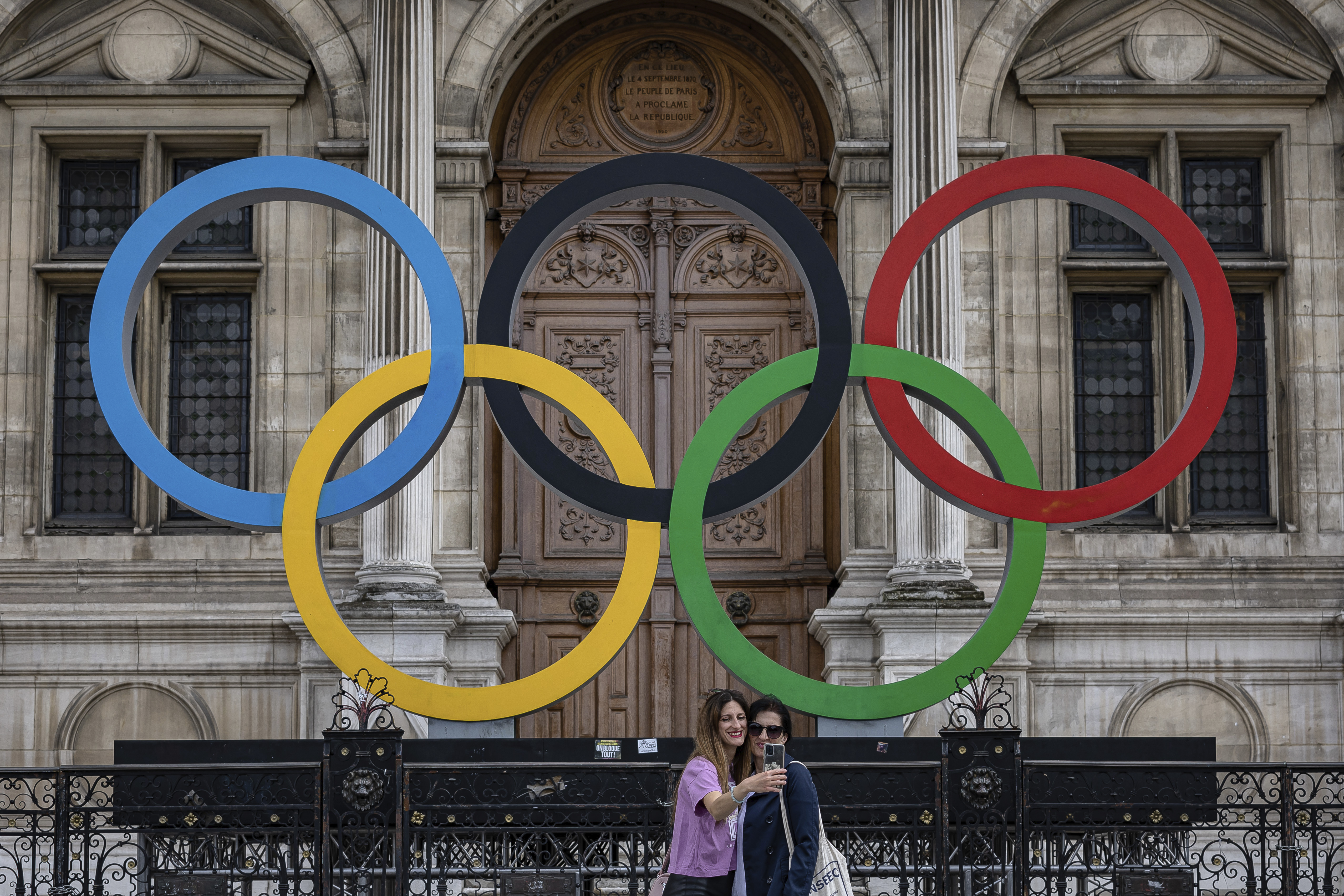 People take a photographs of the Olympic rings in front of the Paris City Hall, in Paris, April 30. Protesters are linking the Paris Games to unpopular pension reforms pushed through by French President Emmanuel Macron.