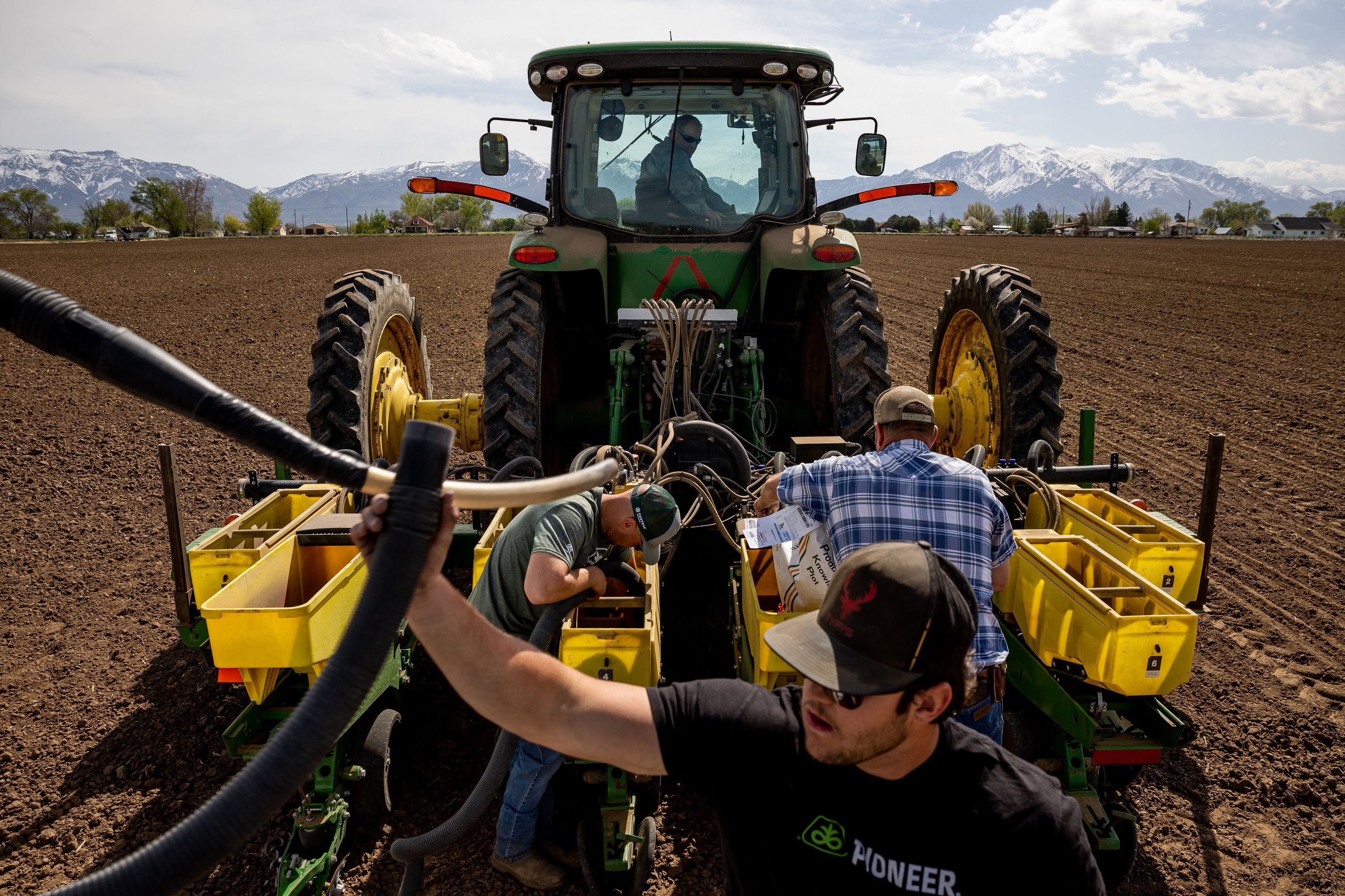 Ron Gibson, owner of Gibson’s Green Acres and president of the Utah Farm Bureau, looks down from the pilot seat of his tractor while Landon Potter, Wyatt Monroe and Shane Monroe switch between different varieties of corn seed in a planter on Gibson’s farm in Ogden on Thursday.
