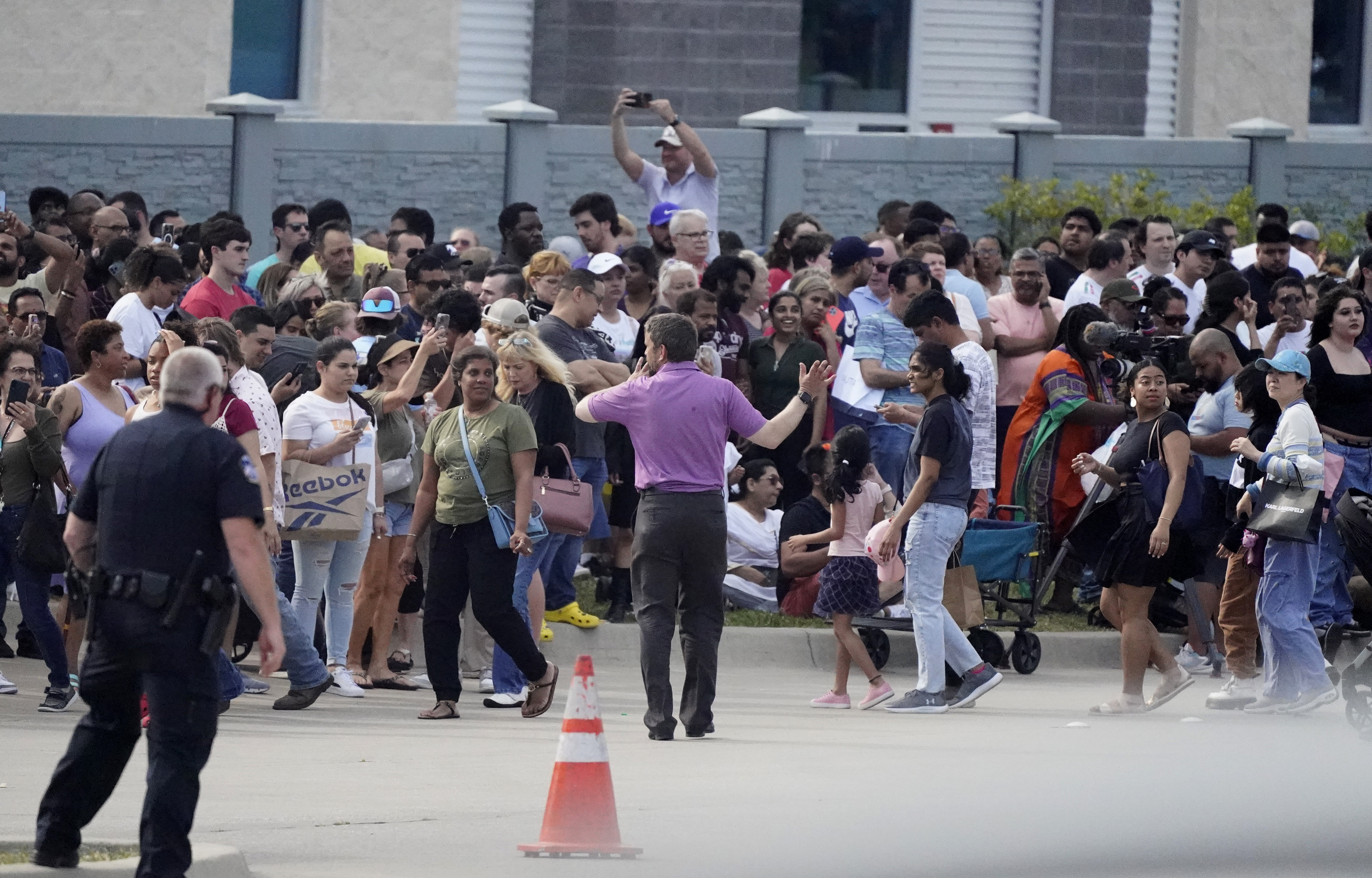 People gather across the street from a shopping center after a shooting Saturday, in Allen, Texas.