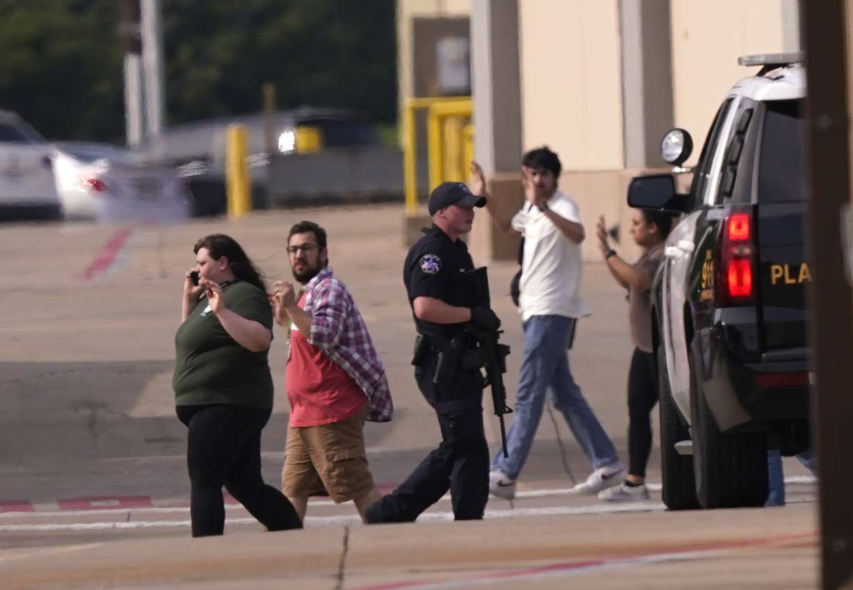 People raise their hands as they leave a shopping center following reports of a shooting, Saturday, in Allen, Texas.
