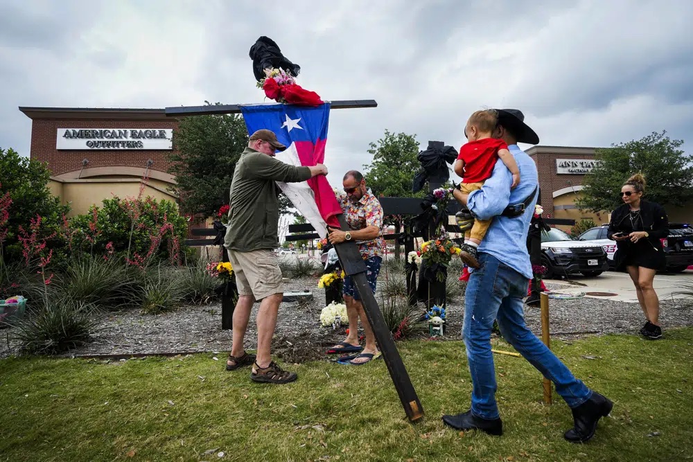 Fred Lowstetter, left, and Israel Gil raise a cross with a Texas flag as they construct a memorial outside an entrance to the mall a day after a mass shooting at Allen Premium Outlets on Sunday in Allen, Texas.