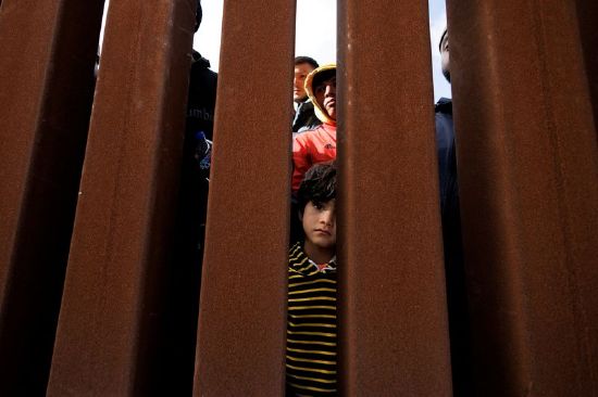 A young boy peers through the border wall near San Diego, California, Monday. The Biden administration and Texas state government are preparing for a possible increase in illegal immigration.