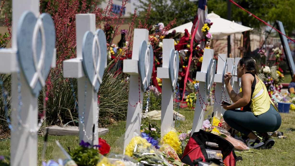 A woman signs a cross that stands by others at a makeshift memorial for the victims of a mass shooting, Monday in Allen, Texas.