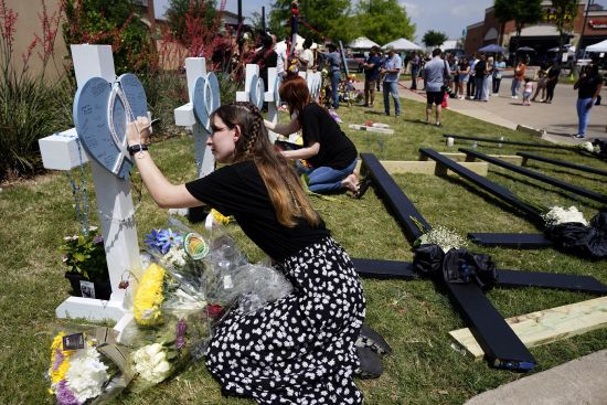 Jennifer Seeley signs a cross that stands by others at a makeshift memorial by the mall where several people were killed several days earlier, Monday in Allen, Texas. Seeley, an employee at the Crocs store at the mall, said she was signing the cross for one of the victims, an acquaintance who worked as a security guard at the mall.