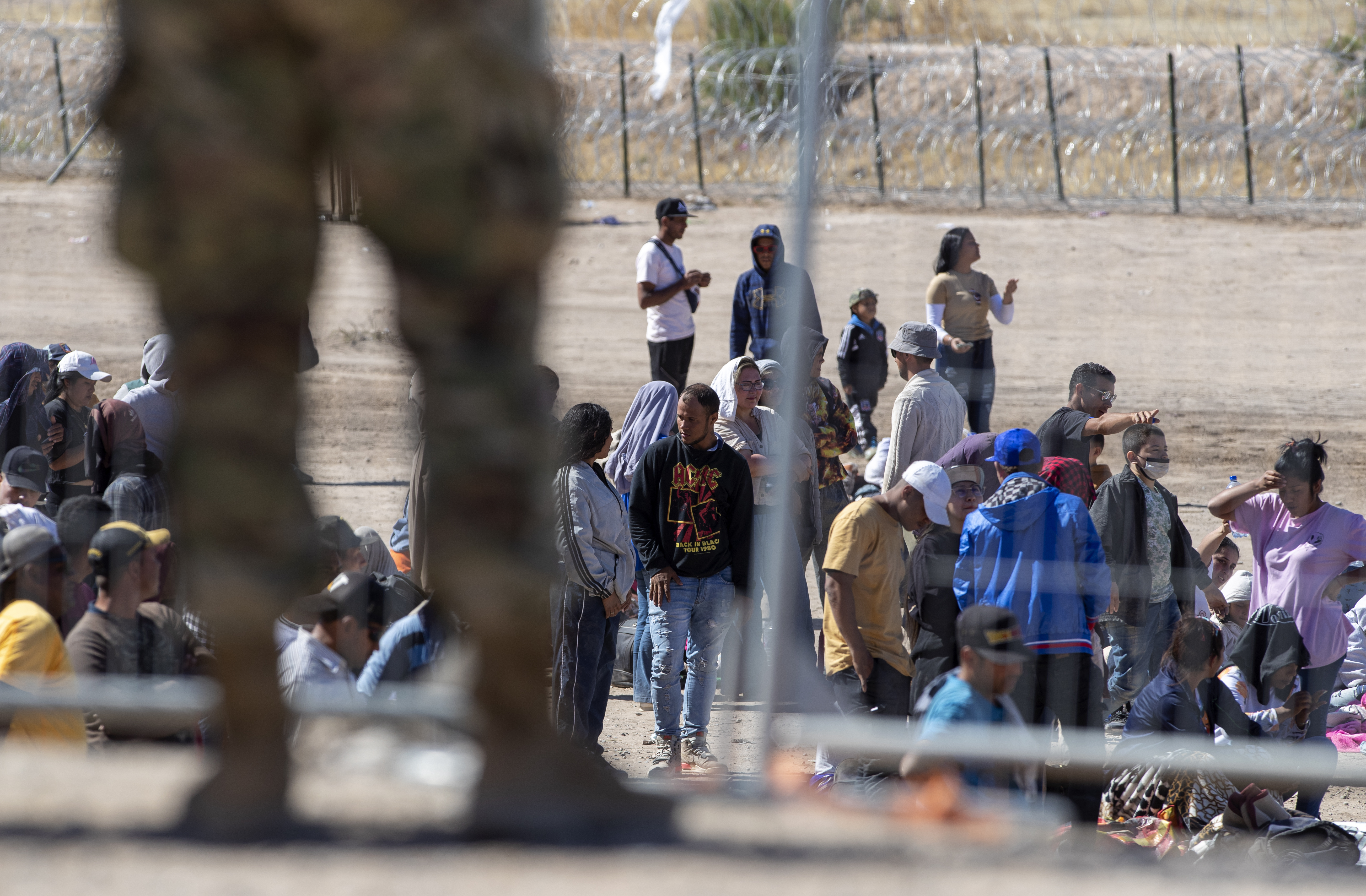 Migrants wait in line adjacent to the border fence under the watch of the Texas National Guard to enter into El Paso, Texas, Wednesday.