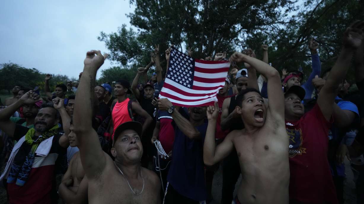 Venezuelan migrants wave a U.S. flag at a television helicopter that flew over the Rio Grande, in Matamoros, Mexico, Friday, a day after pandemic-related asylum restrictions called Title 42 were lifted.