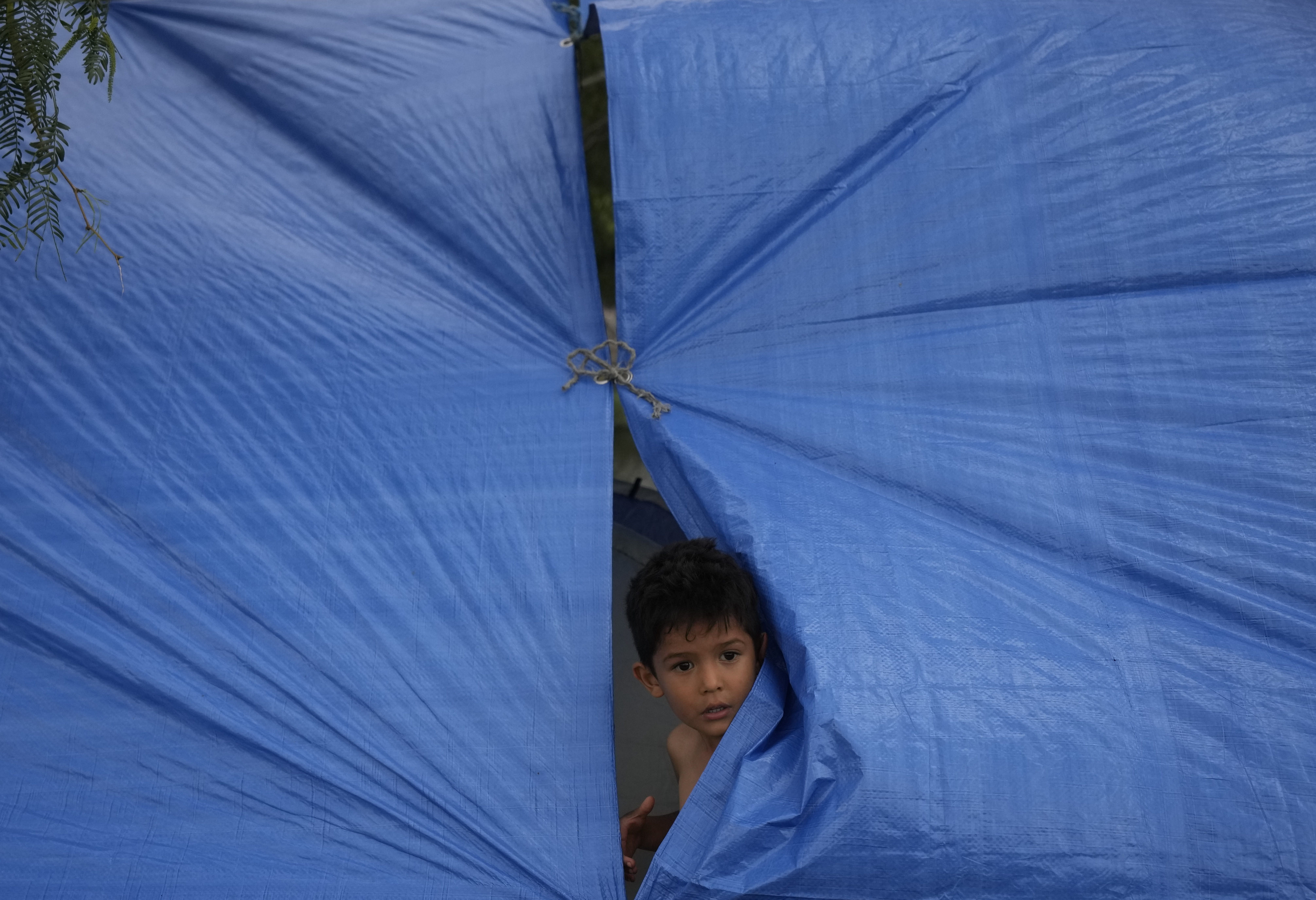 A Venezuelan migrant child looks out from a makeshift tent, constructed by his parents on the the banks of the Rio Grande in Matamoros, Mexico, Friday, a day after pandemic-related asylum restrictions called Title 42 were lifted.