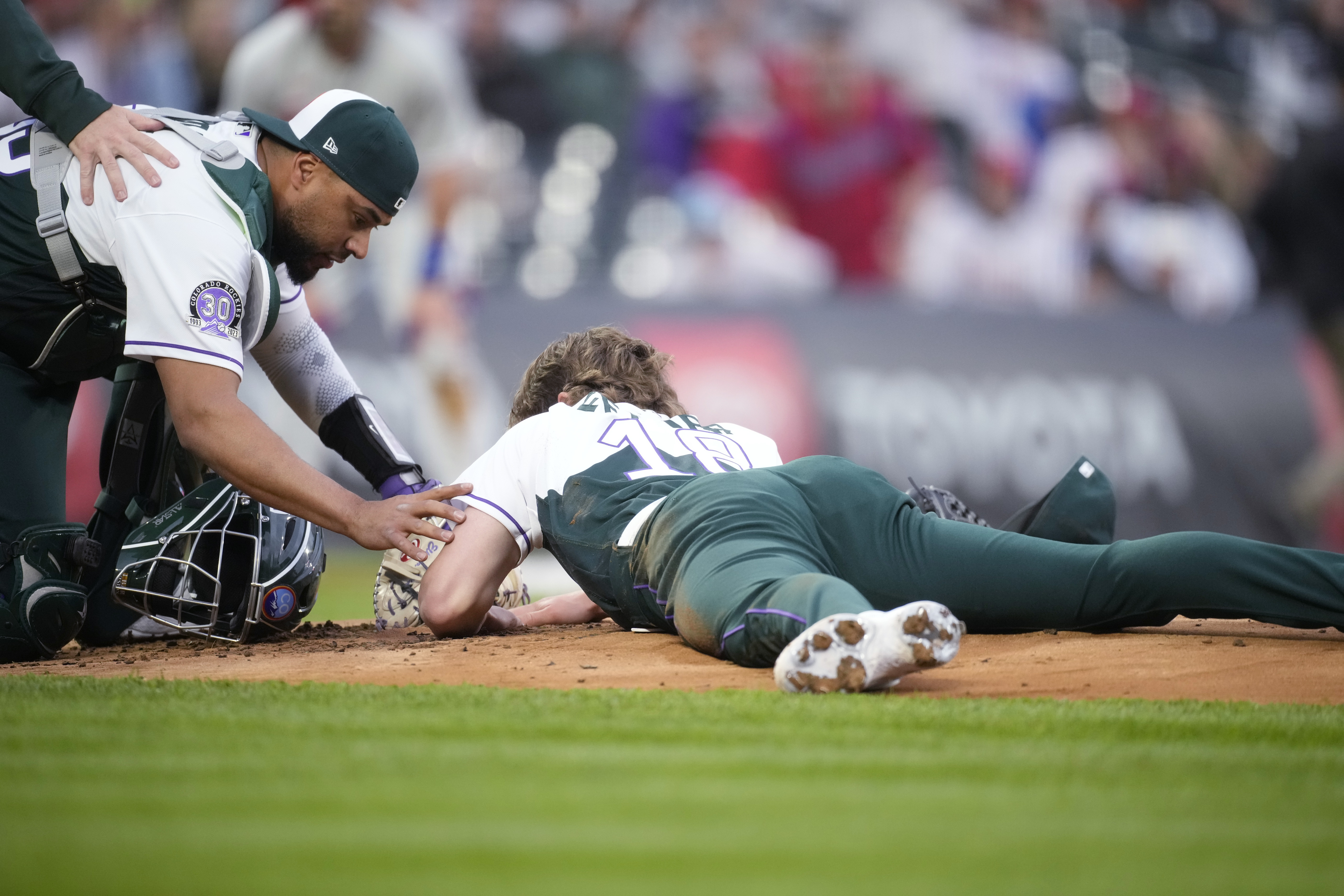 Colorado Rockies catcher Elias Diaz, left, checks on starting pitcher Ryan Feltner, who lies on the mound after getting hit by a single off the bat of Philadelphia Phillies' Nick Castellanos during the second inning of a baseball game Saturday, May 13, 2023, in Denver. 